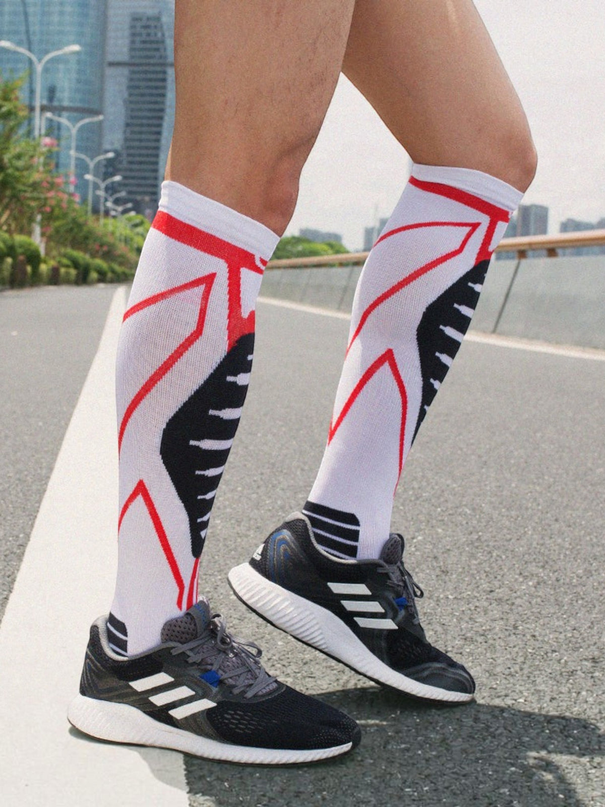 Kotyss knee high compression socks in white with red and black athletic patterns worn by a runner on a road