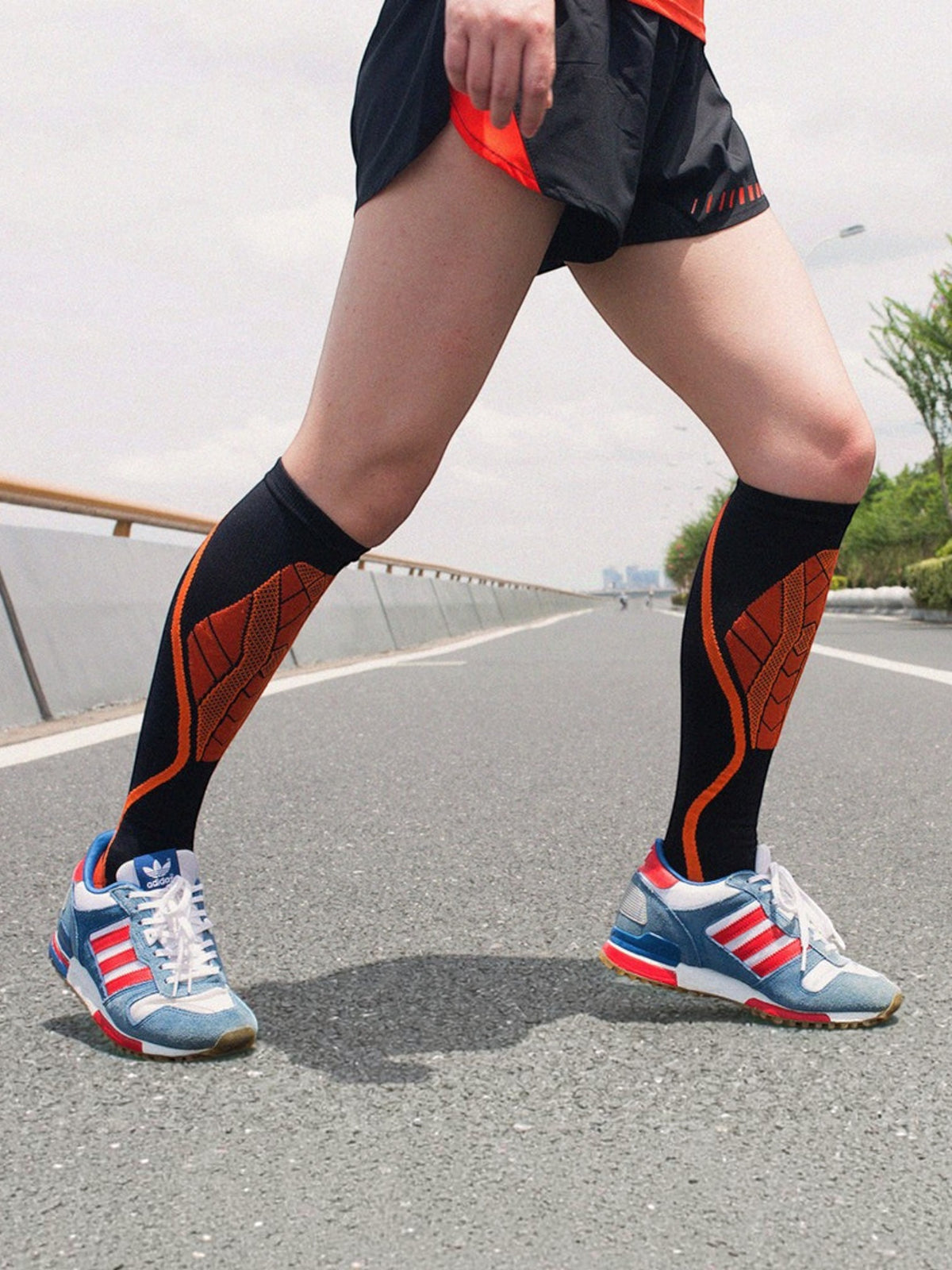 Kotyss knee high athletic compression socks in black and orange worn by a runner on an outdoor road
