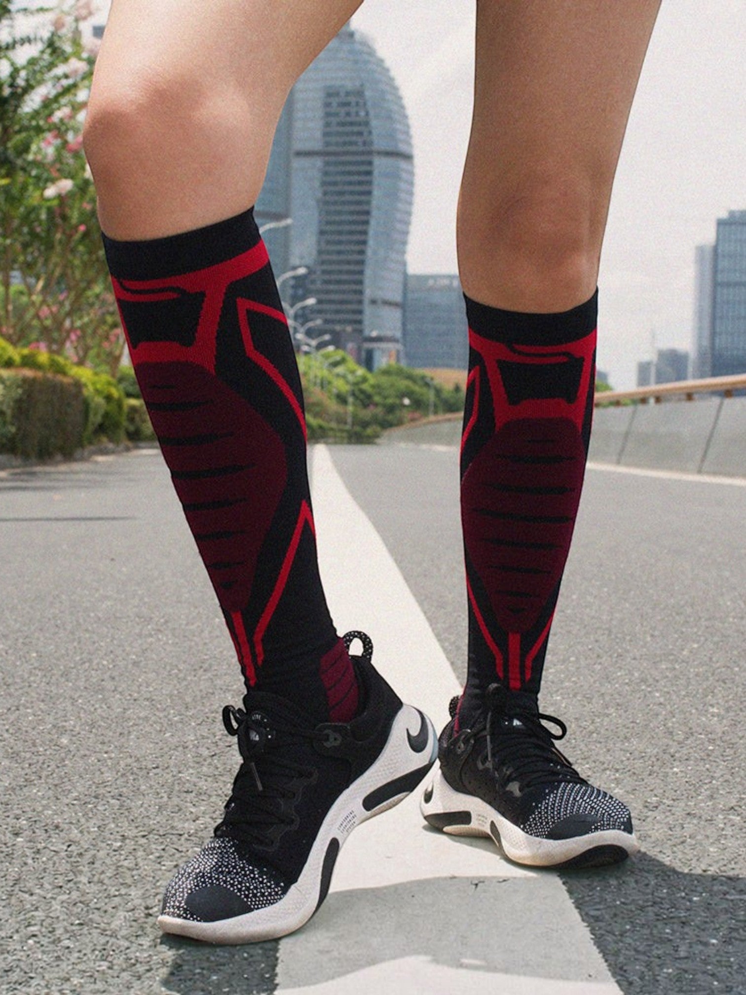 Kotyss knee-high athletic compression socks in black and red with seamless design worn on a city street