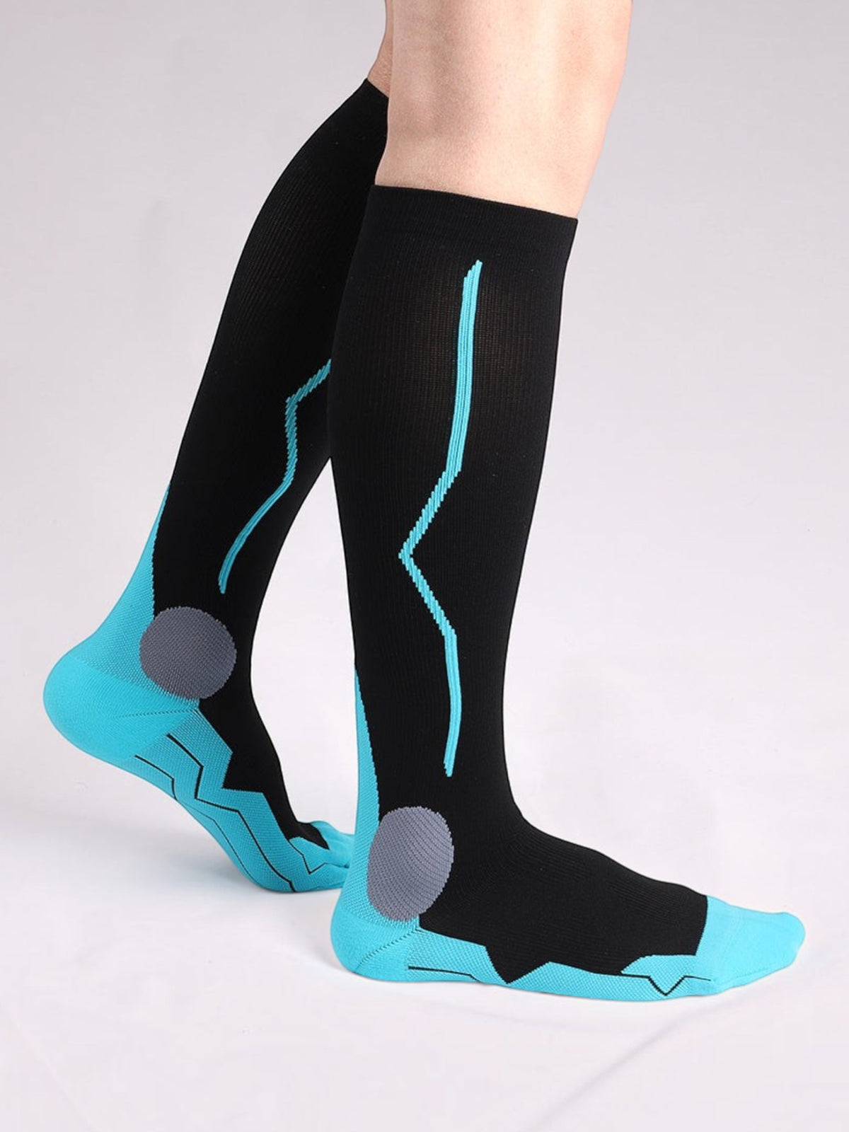 Kotyss black and blue knee-high compression socks with seamless design and targeted padding on a person's legs.