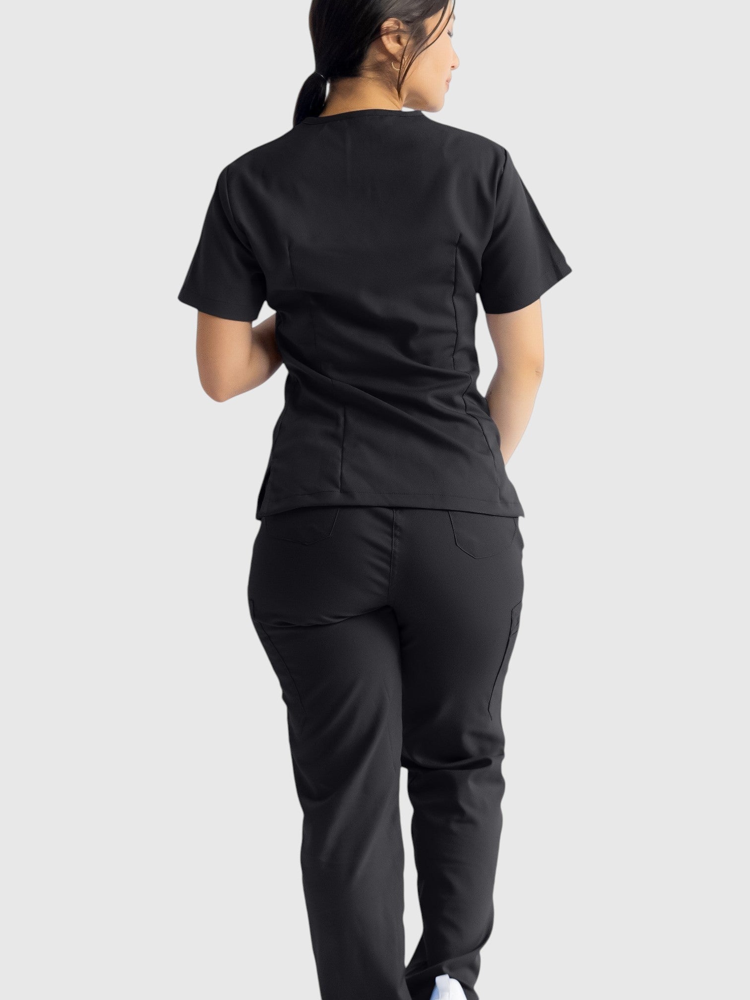 A woman wearing Kotyss black straight cut medical scrub pants and matching top, showing a back view.