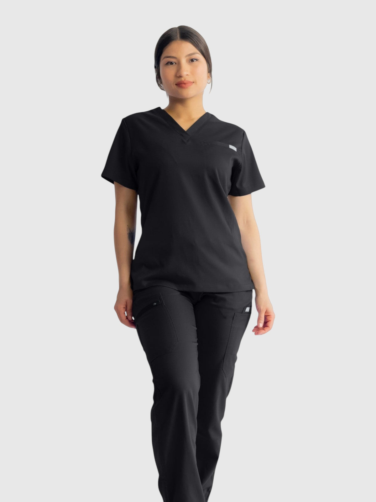 A woman wearing Kotyss black straight cut medical scrub pants and matching v-neck top with multiple utility pockets.
