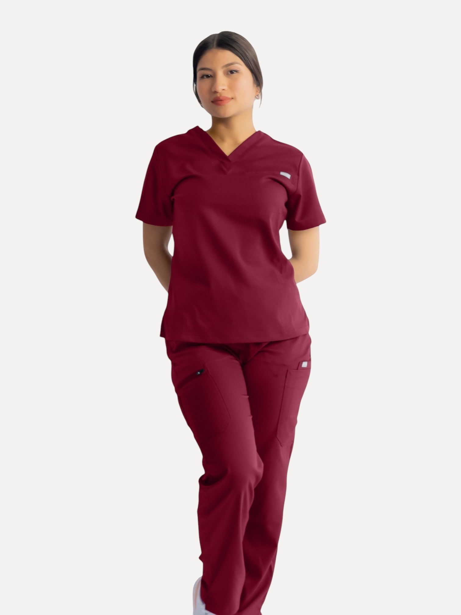 A woman wearing a Kotyss burgundy straight cut scrub set with multiple pockets, made from breathable stretch fabric.