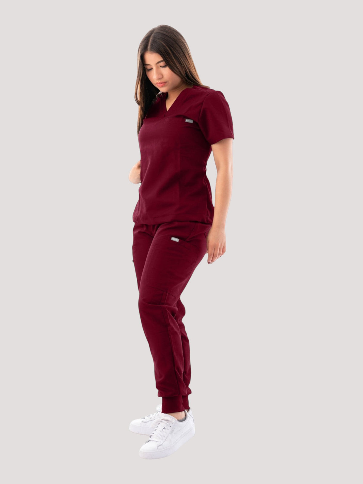 A woman wearing a burgundy Kotyss V-neck scrub top and matching jogger pants with multiple pockets.