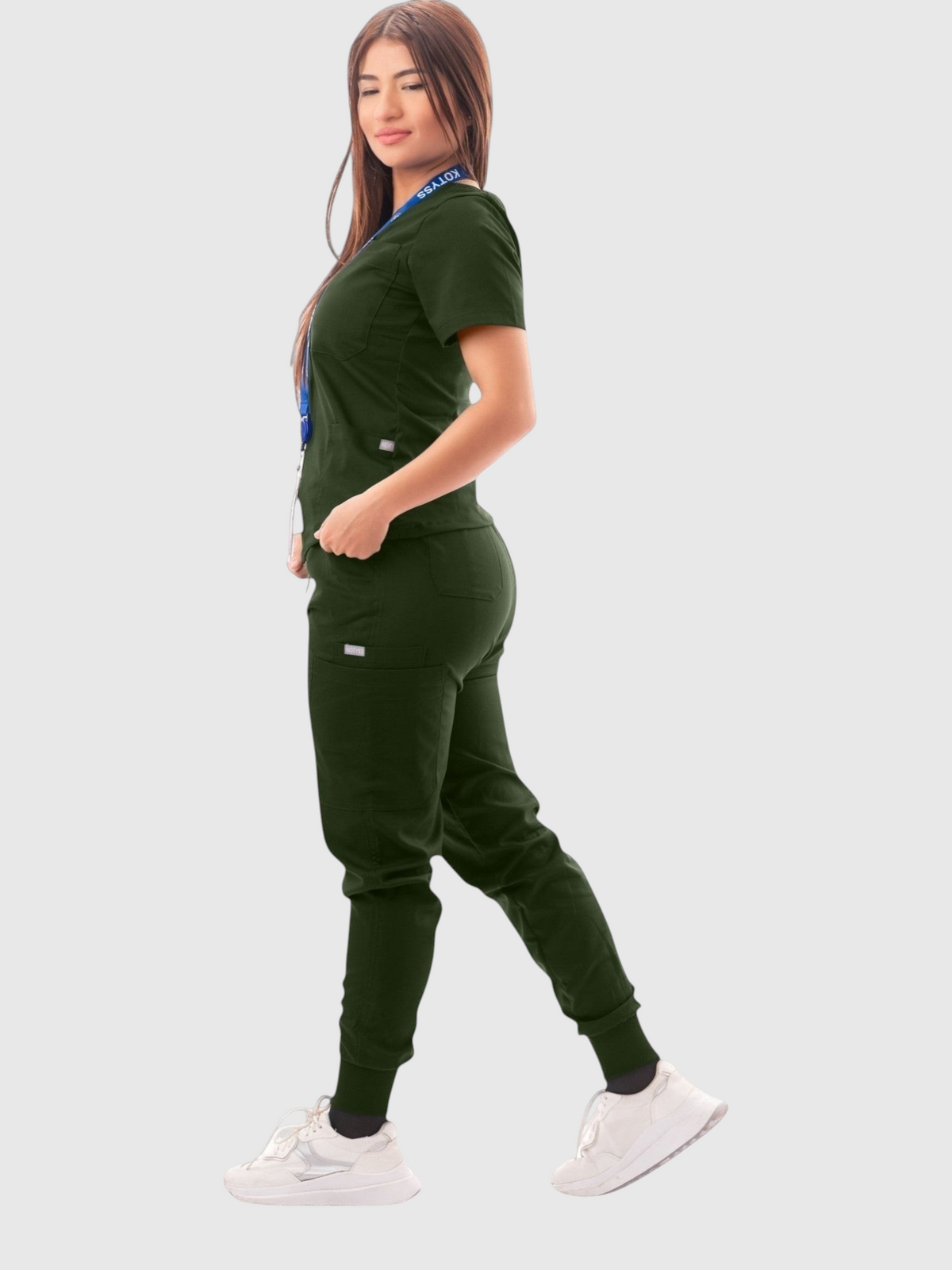A woman wearing a dark green Kotyss V-neck scrub top and matching multi-pocket jogger pants in a studio setting.