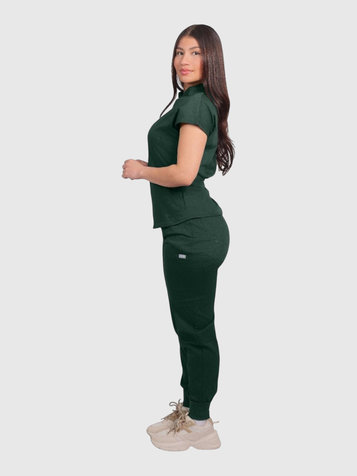A woman wearing a dark green Kotyss collared scrub top and matching jogger pants with 4-way stretch fabric.