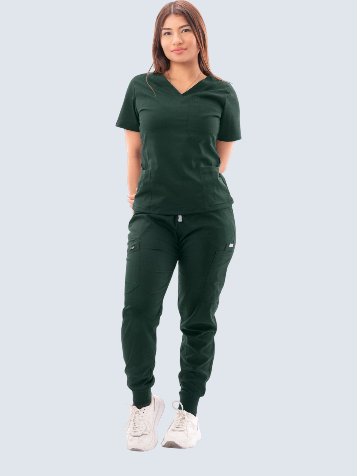 Woman wearing a dark green Kotyss V-neck scrub top and matching multi-pocket jogger pants with white sneakers.
