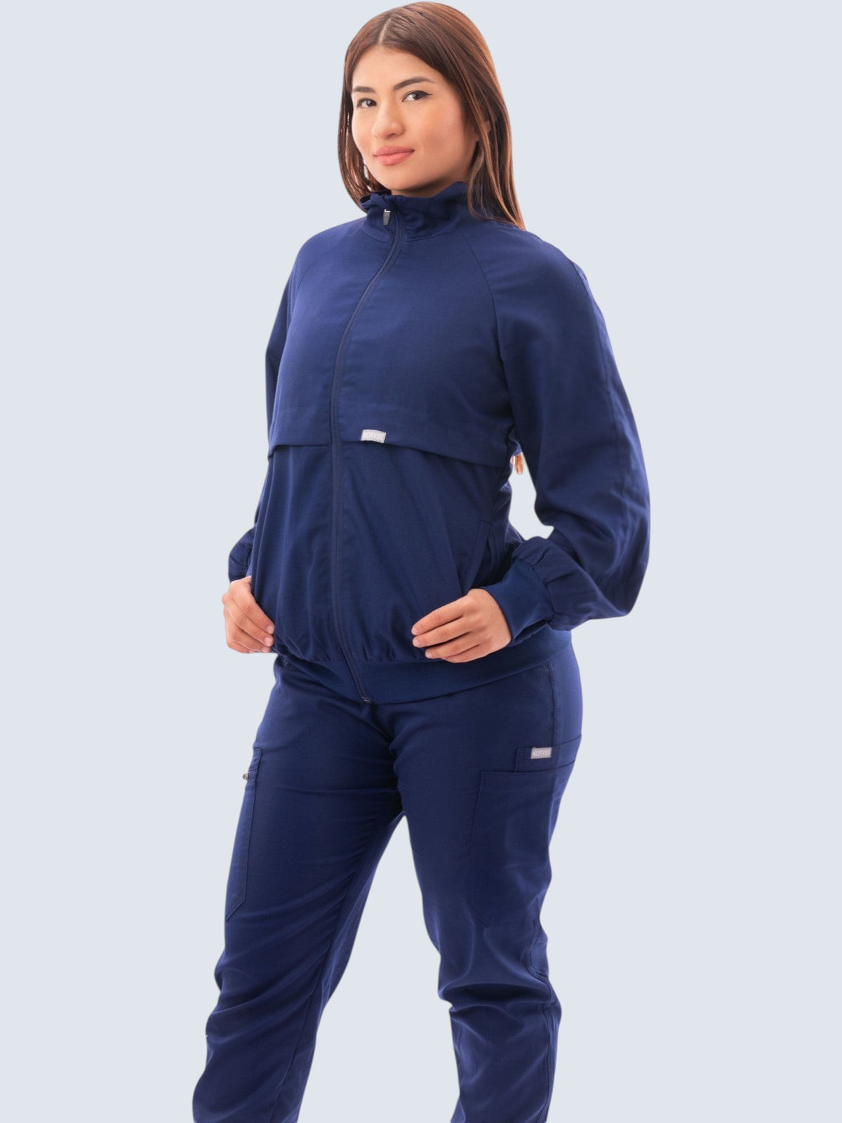 A model wearing a navy blue Kotyss women's scrub jacket with a high windbreaker neck and ribbed knit cuffs.