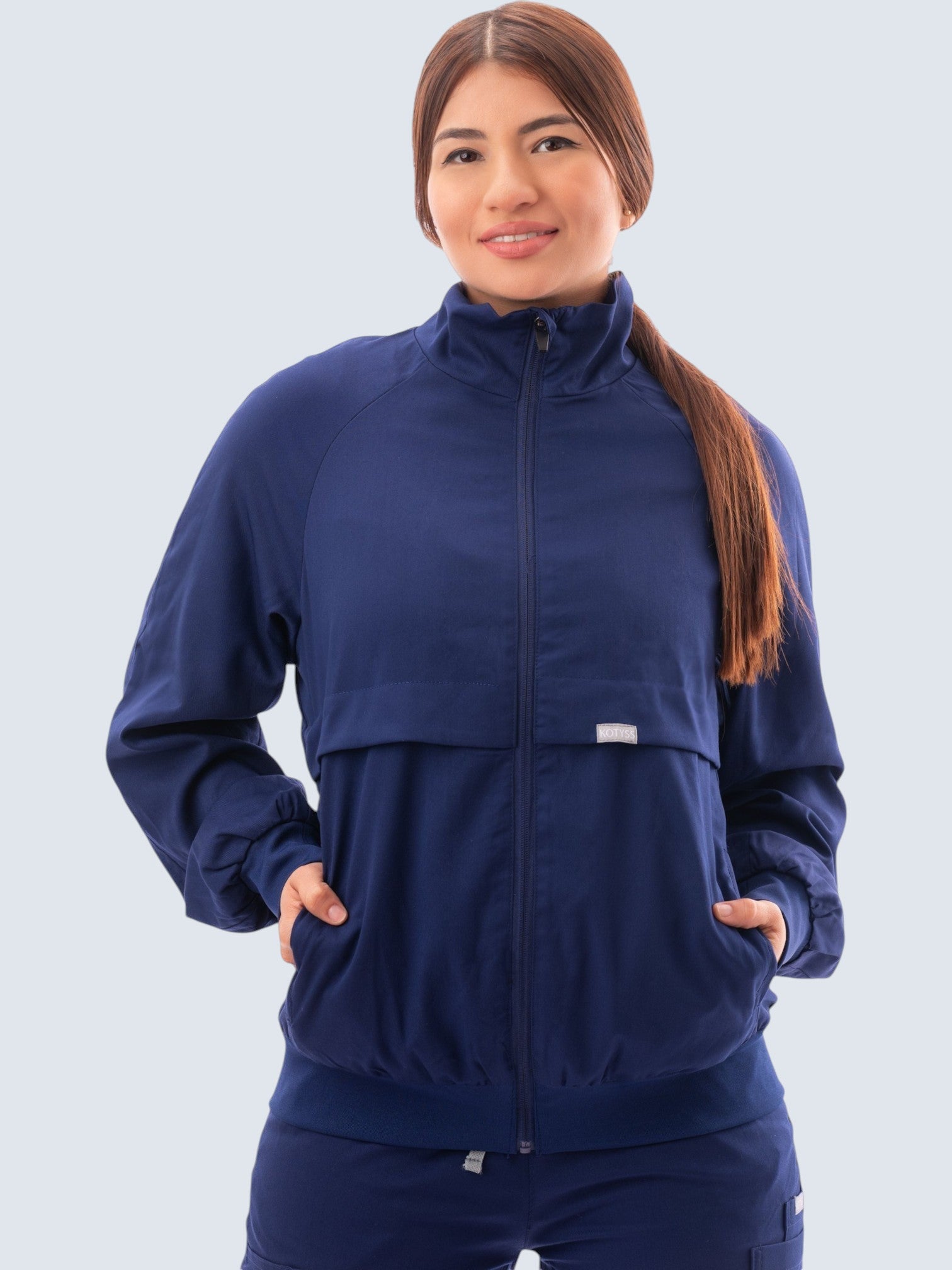 A woman wearing a navy blue Kotyss scrub jacket with a high windbreaker neck, zip front, and ribbed knit cuffs.