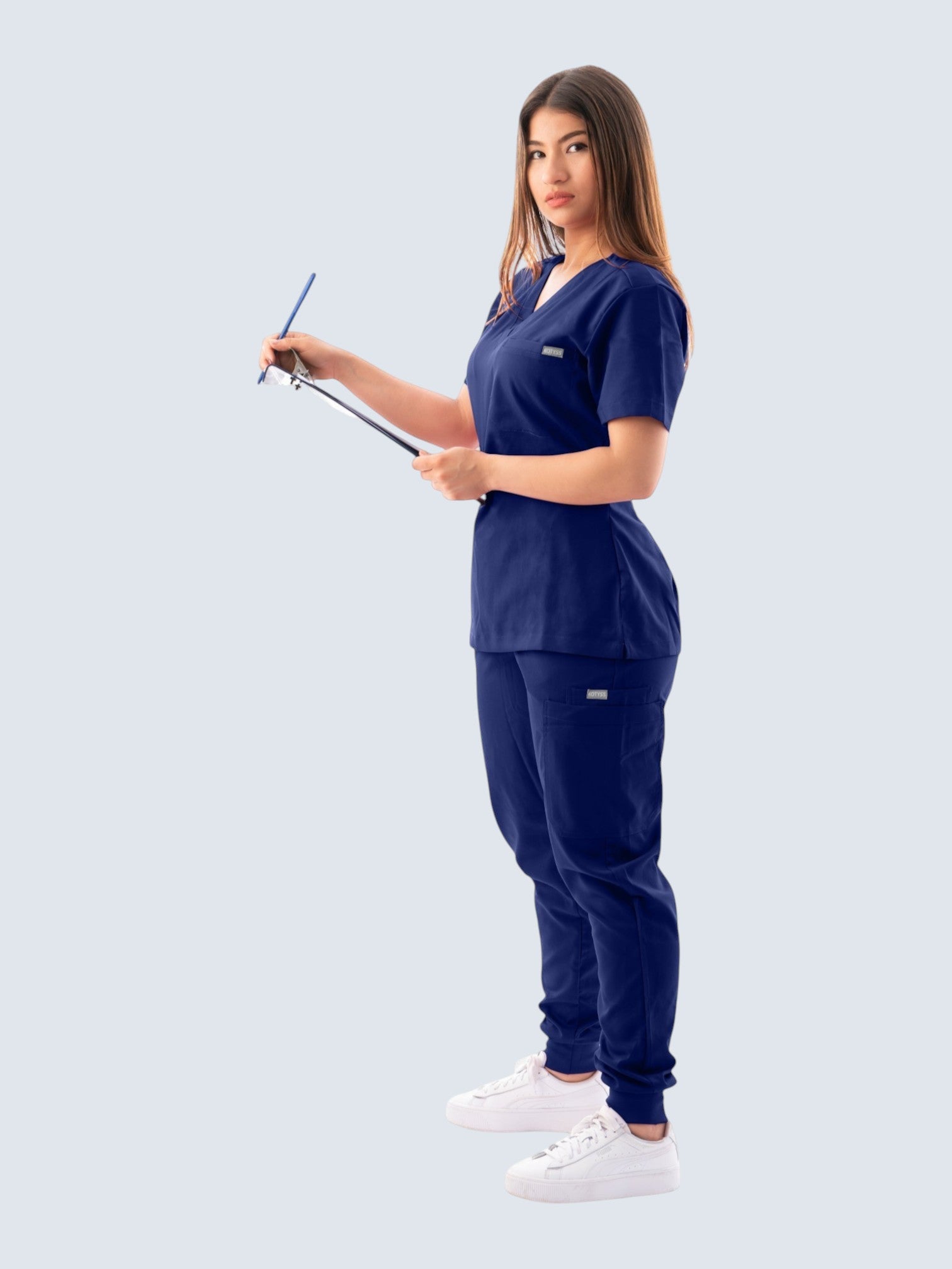 Kotyss women's navy blue V-neck scrub top and jogger pants set with multiple pockets on a model holding a clipboard.