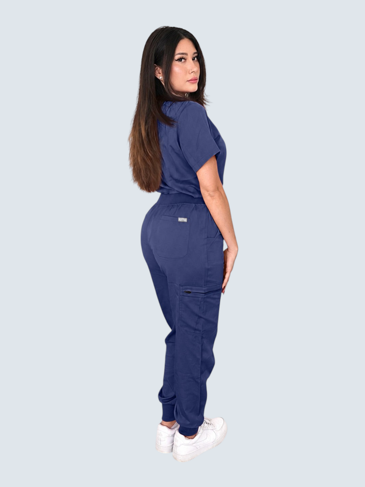 Kotyss women's navy blue V-neck scrub top and multi-pocket jogger pants set on a model, side view.