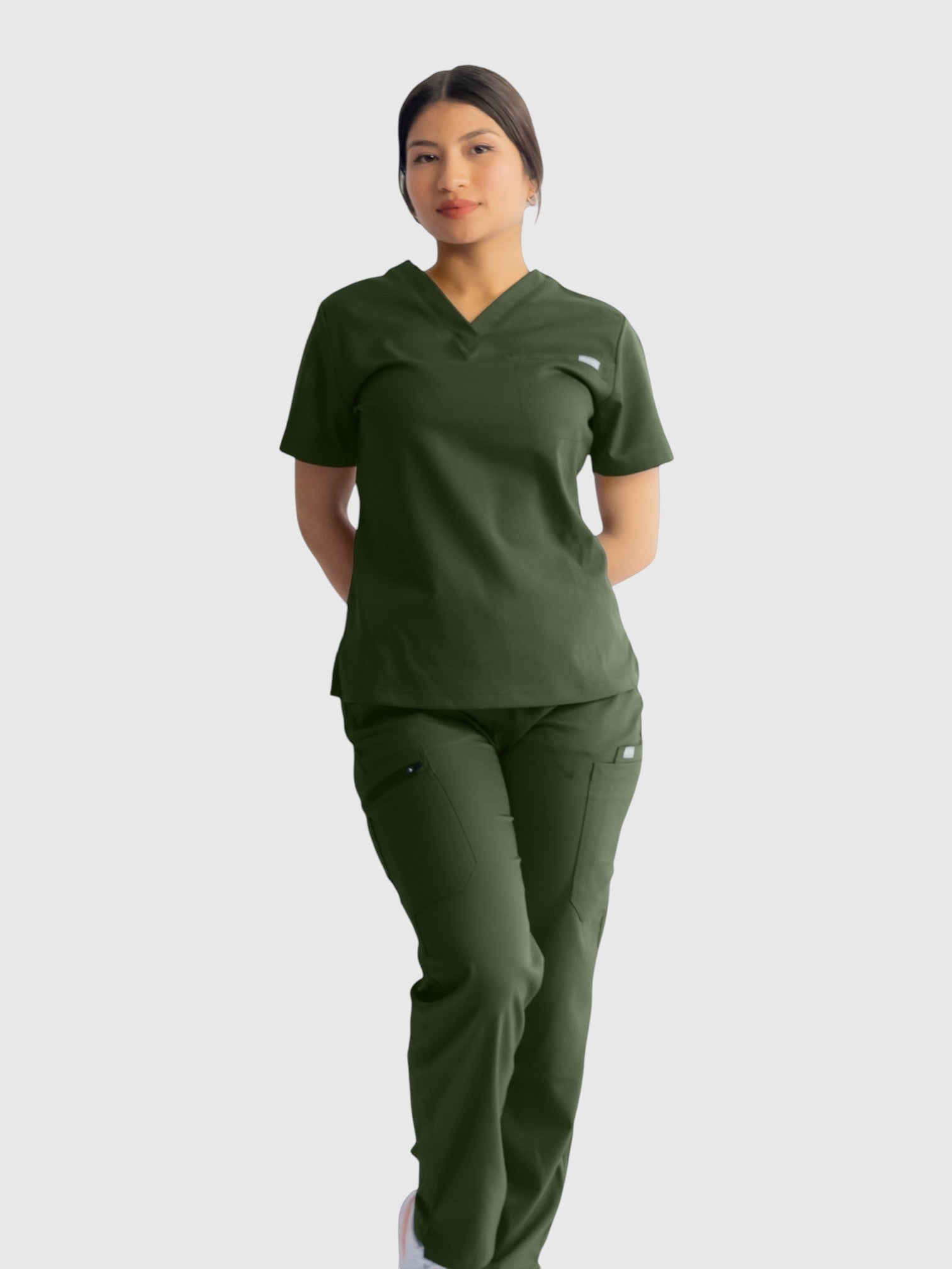 A woman wearing Kotyss olive green straight cut scrub pants and matching V-neck top, featuring multiple utility pockets.