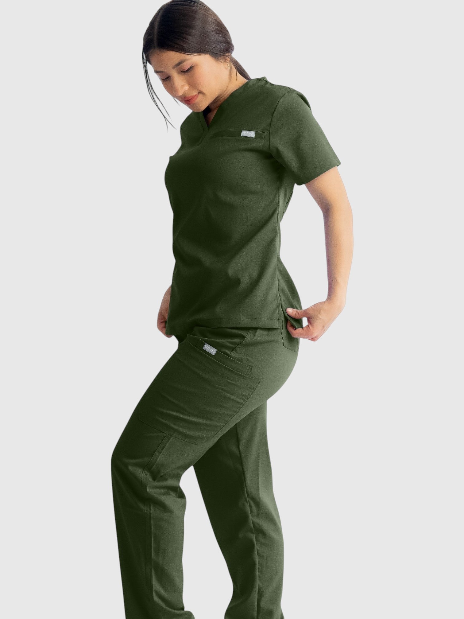 A woman wearing Kotyss olive green straight cut scrub pants and matching top, featuring multiple utility pockets.