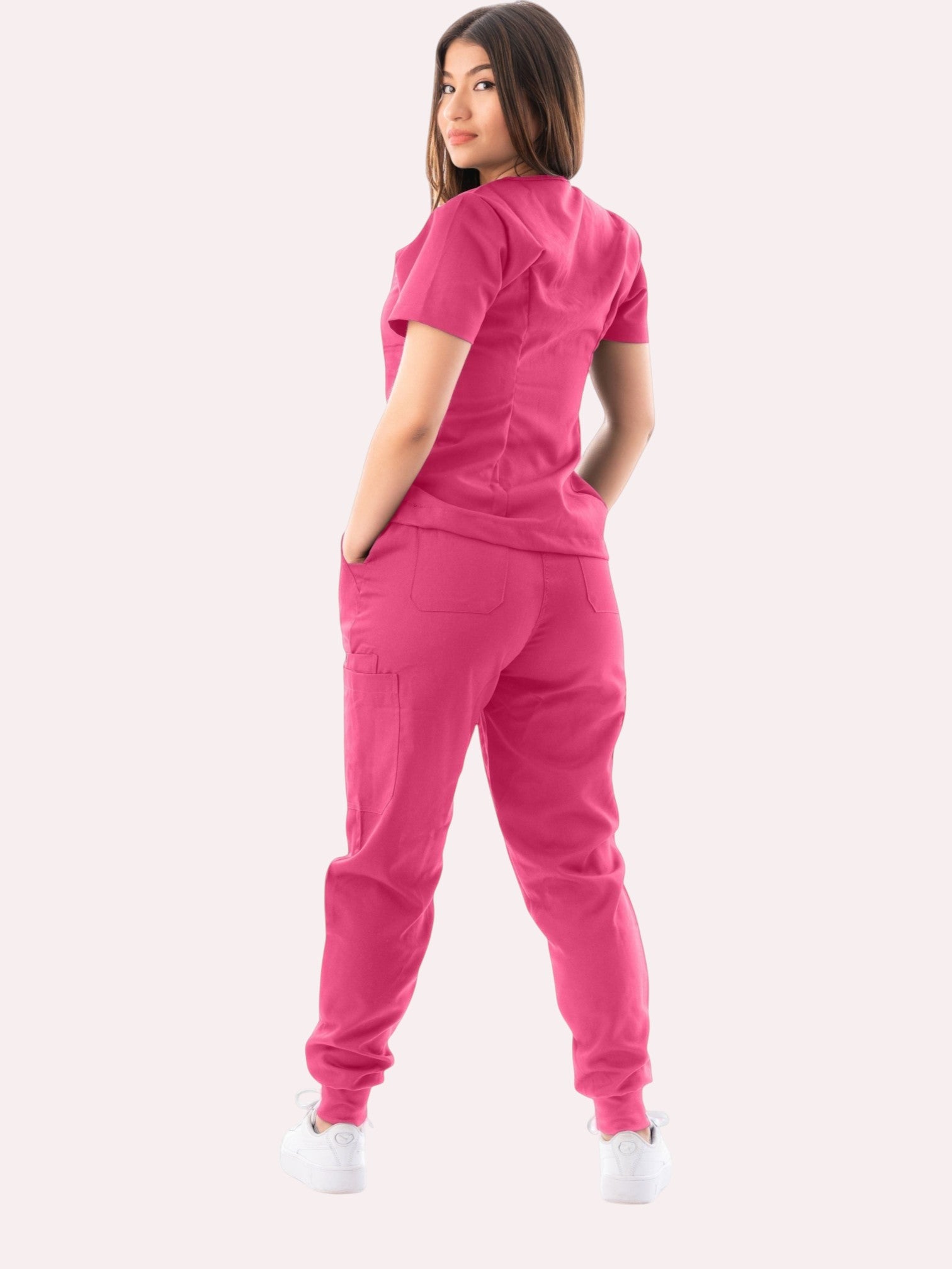 A woman wearing a vibrant pink Kotyss V-neck scrub top and matching multi-pocket jogger pants, back view.