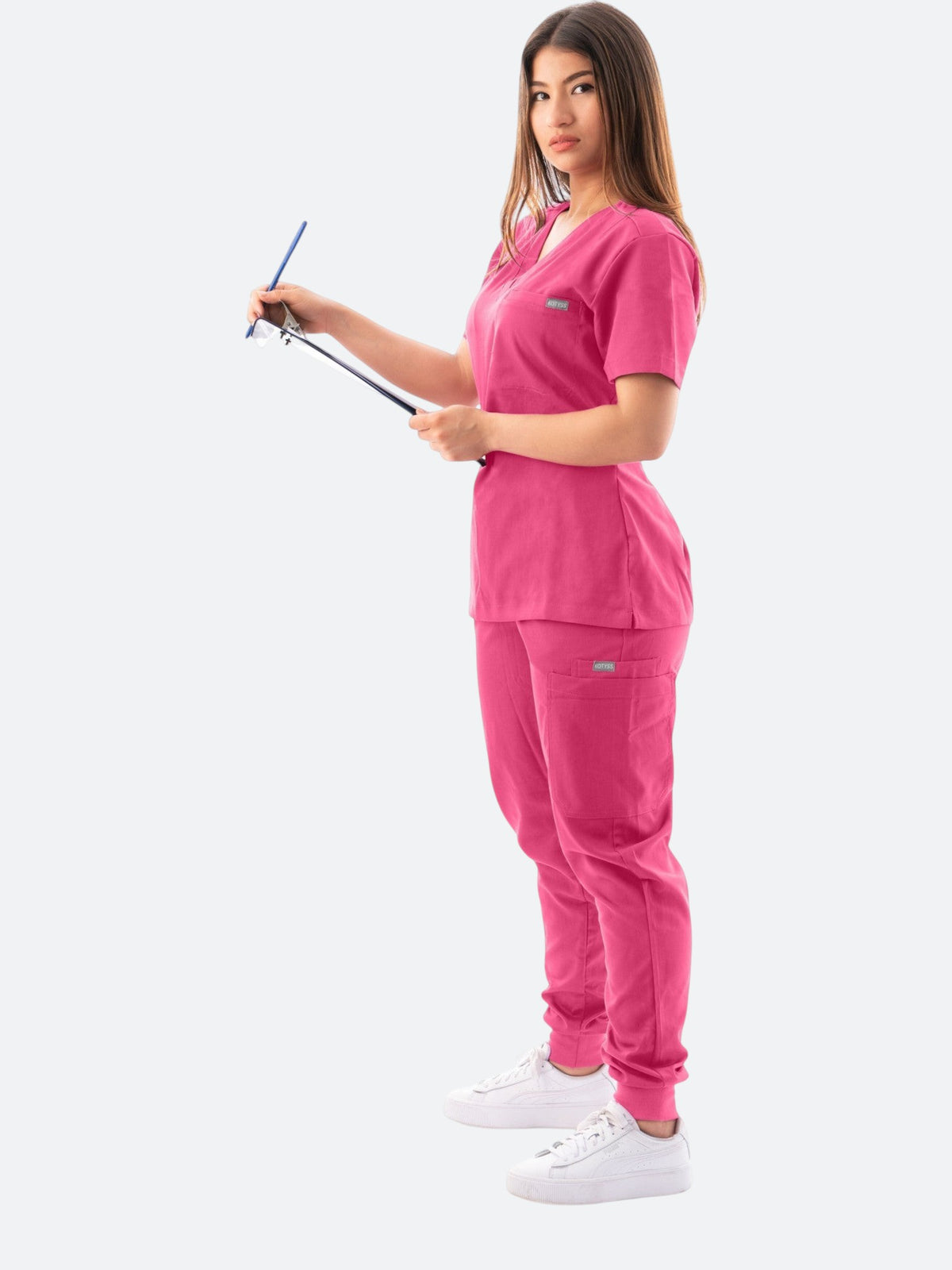 Kotyss women's pink V-neck scrub top and jogger pants set with multiple pockets, worn by a model holding a clipboard.