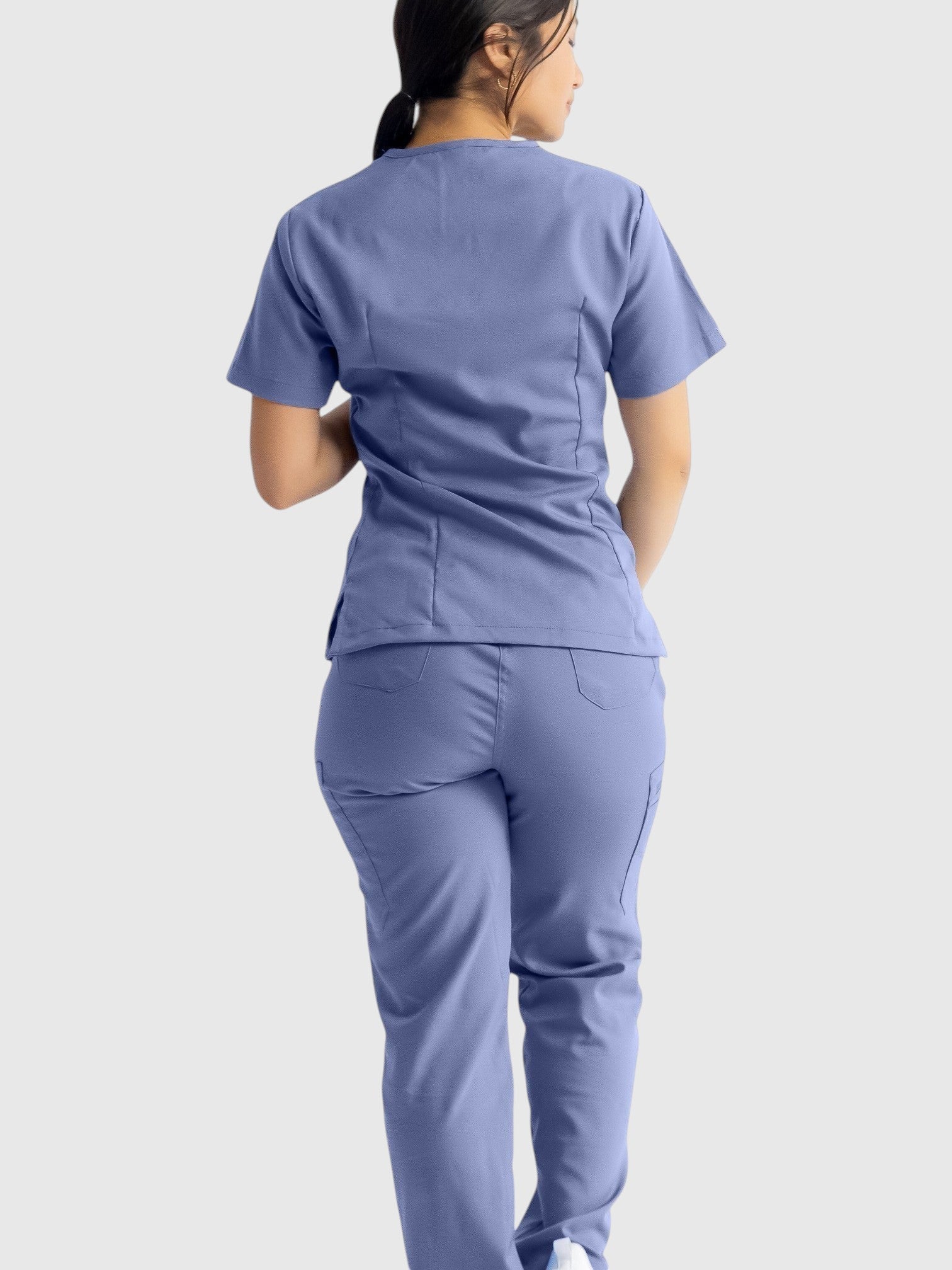 A woman wearing Kotyss straight cut medical scrub pants and matching top in periwinkle blue, back view.