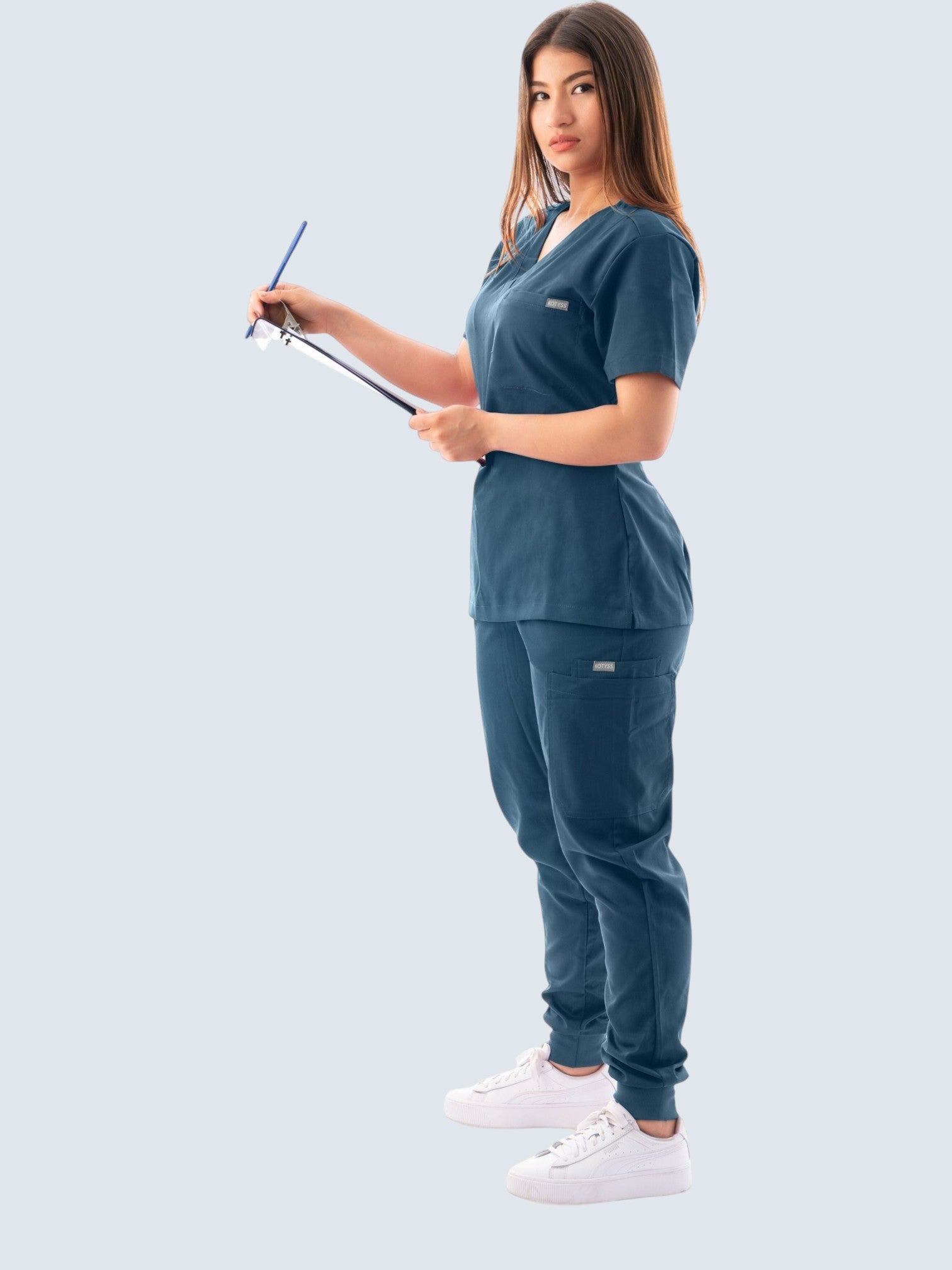 Kotyss women's teal blue V-neck scrub top and jogger pants set with multiple pockets worn by a healthcare professional