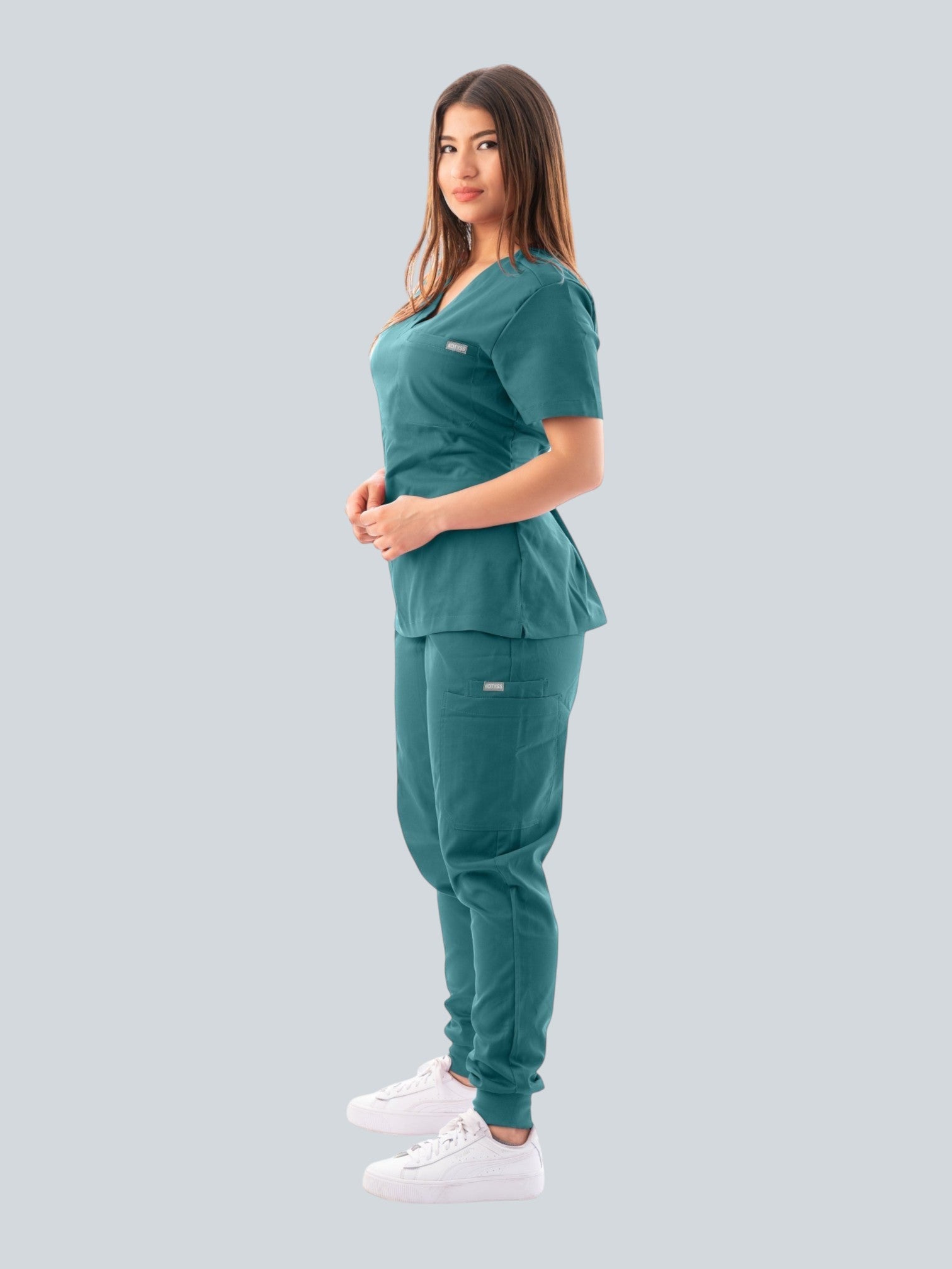 Kotyss women's teal V-neck scrub top and jogger pants set with multiple pockets, worn by a model in profile view.