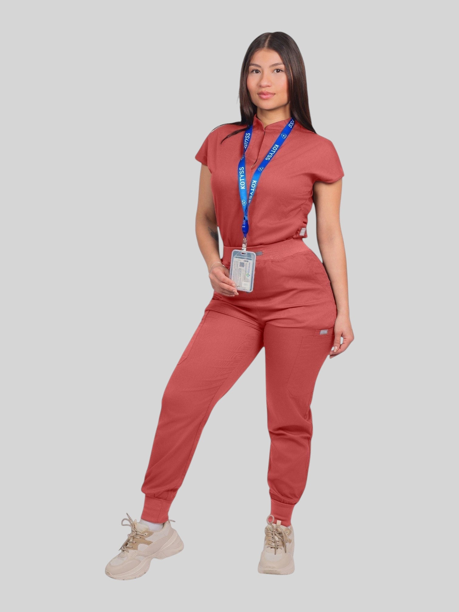 A woman wearing a terracotta Kotyss collared scrub top and matching jogger pants with multiple pockets.