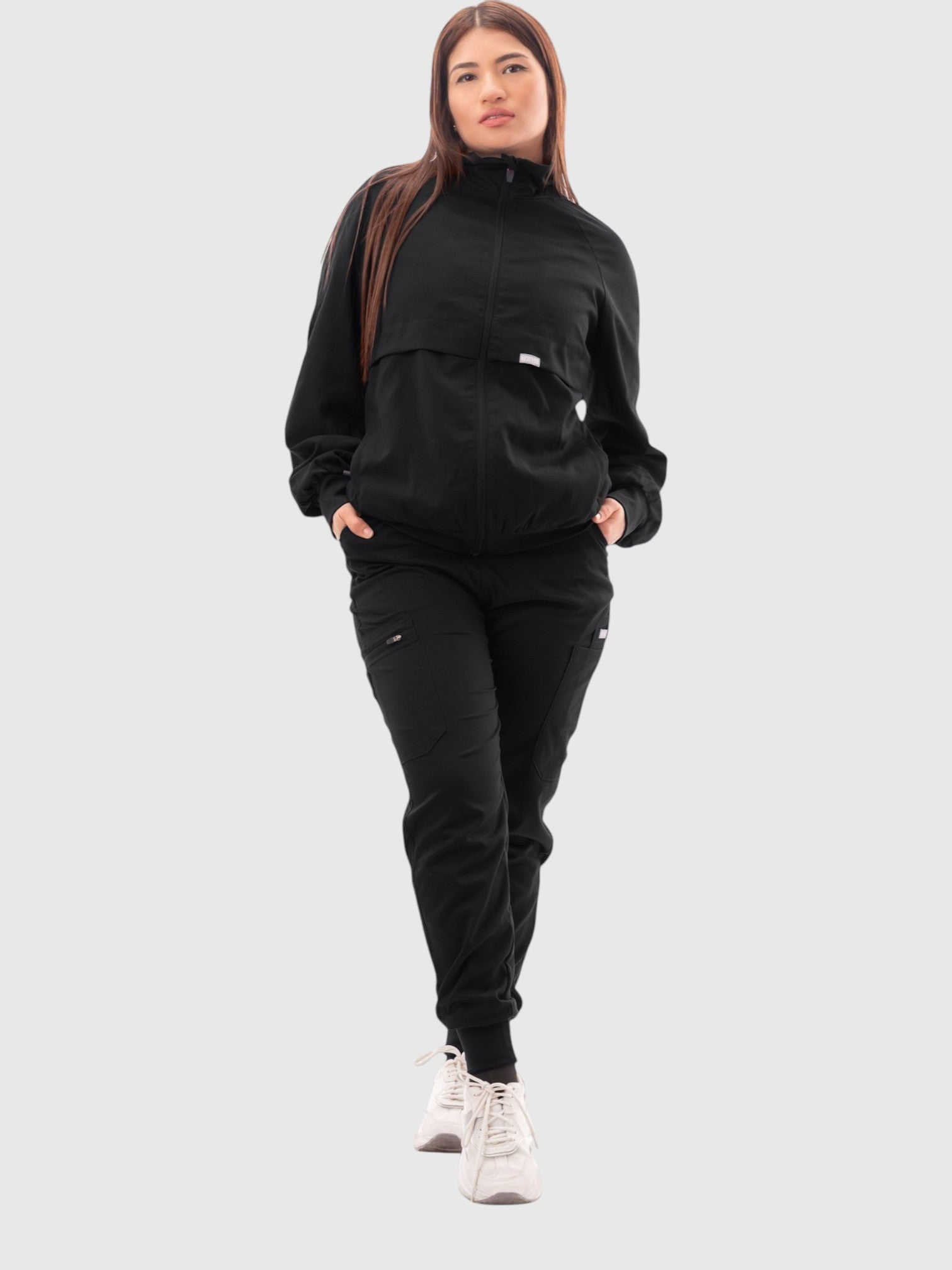 Kotyss women's black scrub jacket with a high windbreaker neck, ribbed cuffs, and pockets, worn by a female model.