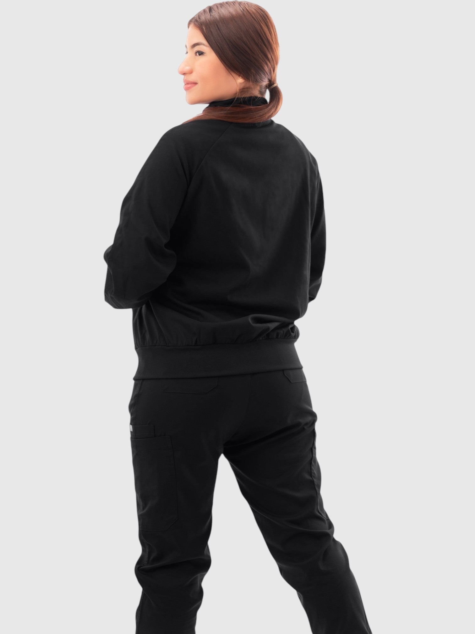 Kotyss women's black scrub jacket with high windbreaker neck and ribbed cuffs, shown from the back on a model.