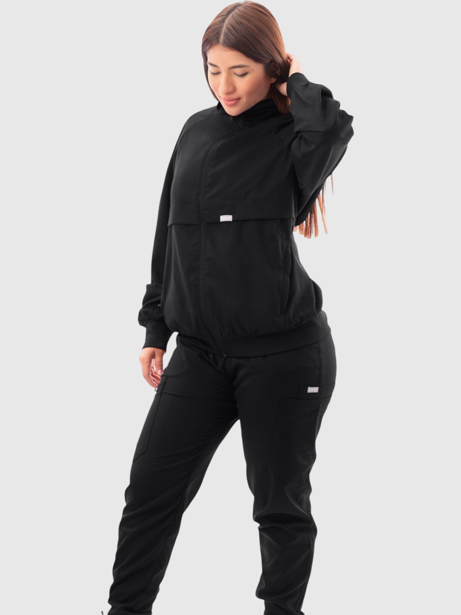 Kotyss women's black scrub jacket with high windbreaker neck, ribbed cuffs, and moisture-wicking fabric on a model.