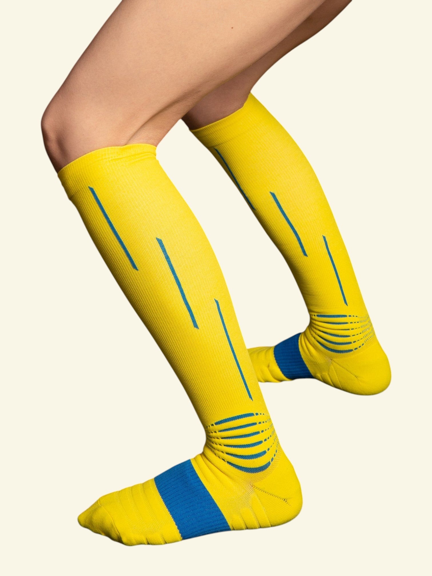 Kotyss yellow knee-high compression socks with blue accents and seamless design worn on legs for support.
