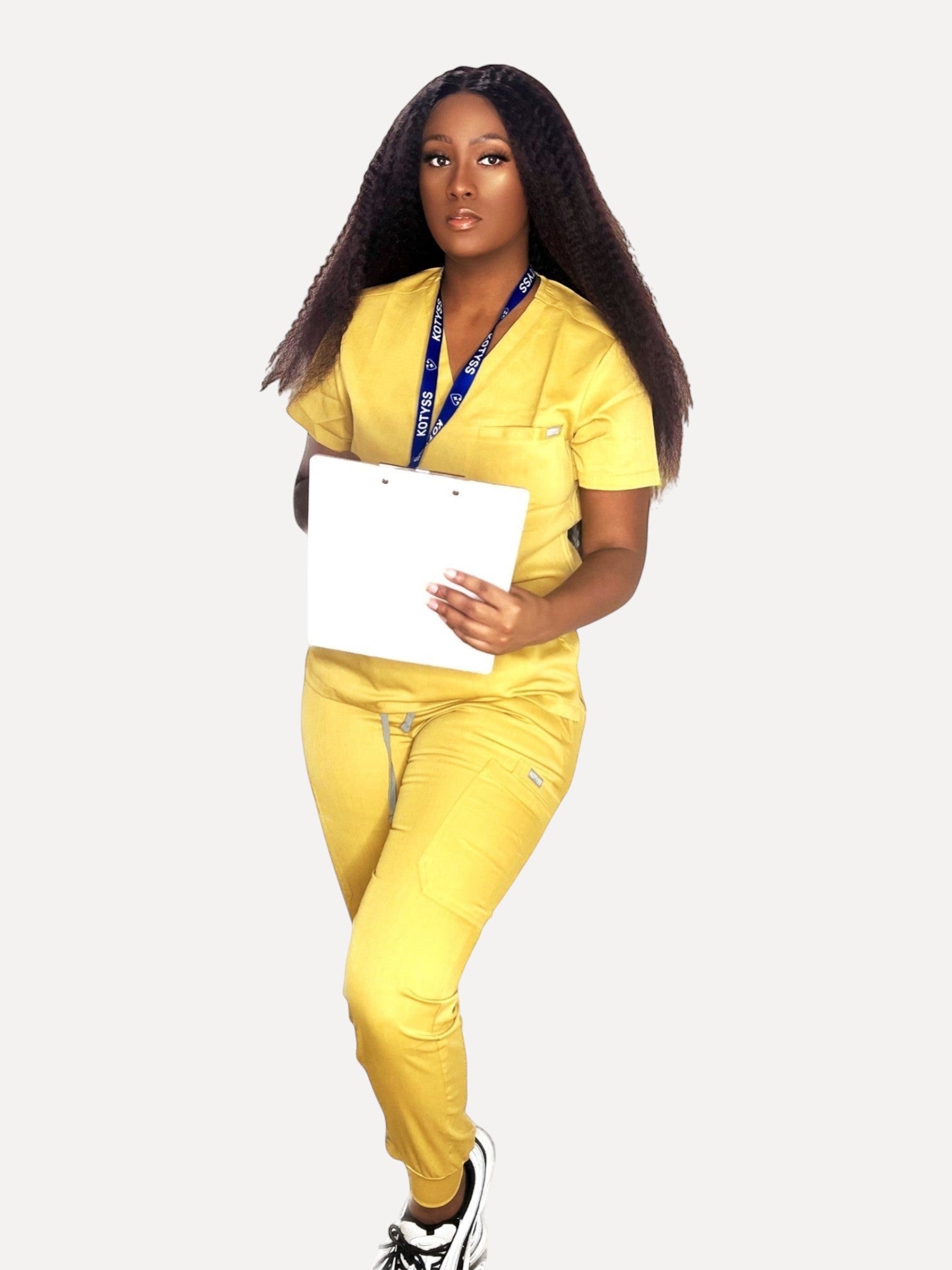 Model wearing a yellow Kotyss V-neck scrub top and jogger pants with a clipboard, featuring 4-way stretch fabric.