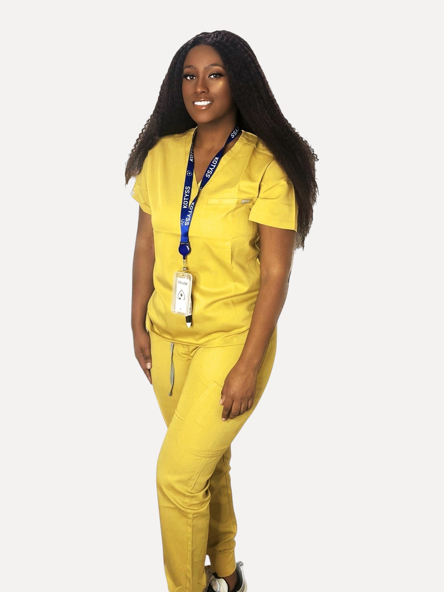 A woman wearing a yellow Kotyss V-neck scrub top and matching jogger pants with a branded lanyard.