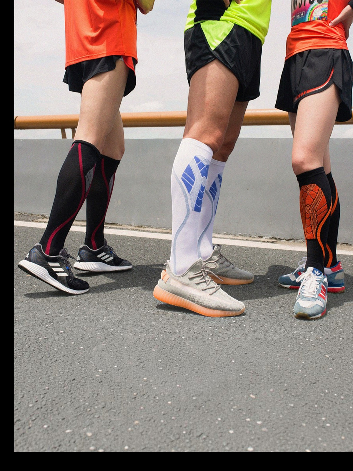 Three runners wearing Kotyss knee-high compression socks in black, white, and orange with athletic sneakers.