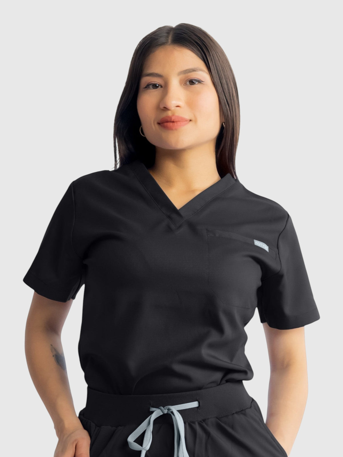 Kotyss black medical scrub top and pants set with V-neck, worn by a woman against a white background.