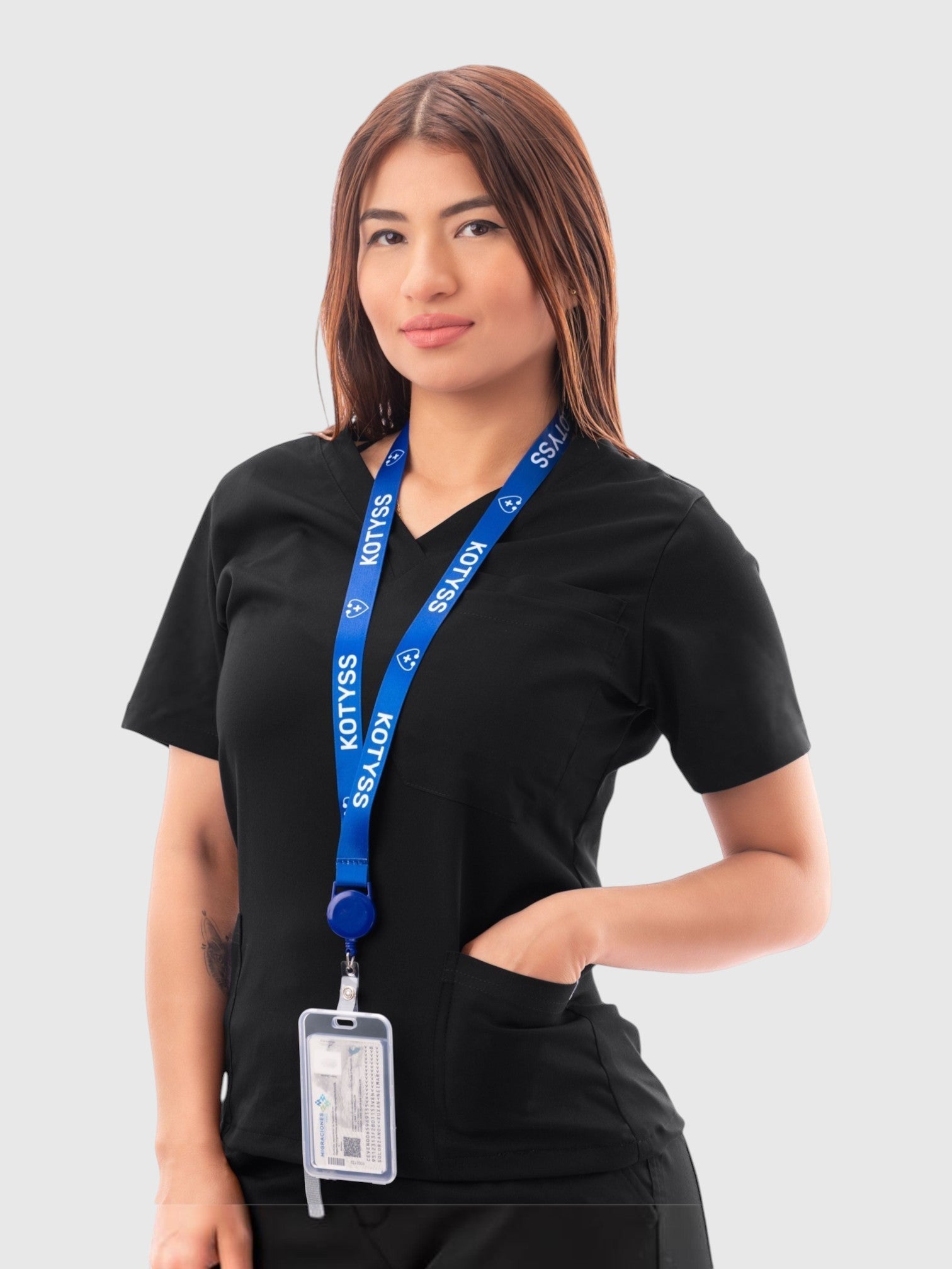 A woman wearing a black Kotyss V-neck medical scrub top with a blue branded lanyard against a white background.
