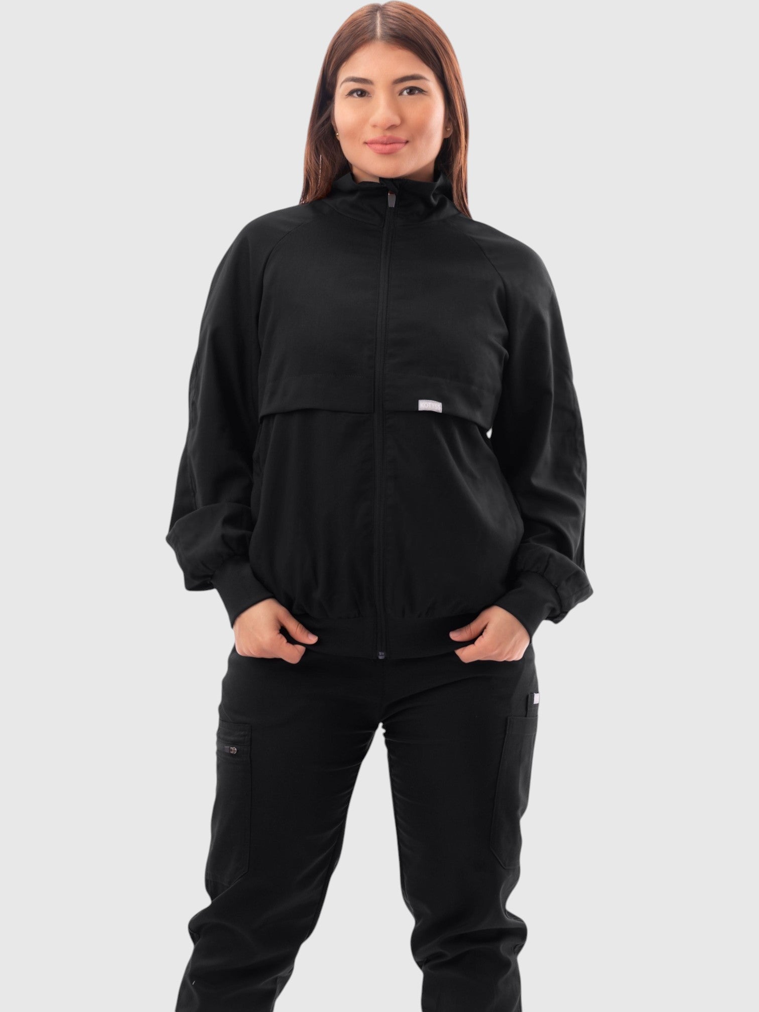 Kotyss women's black scrub jacket with a high windbreaker neck, ribbed cuffs, and a tailored professional fit.