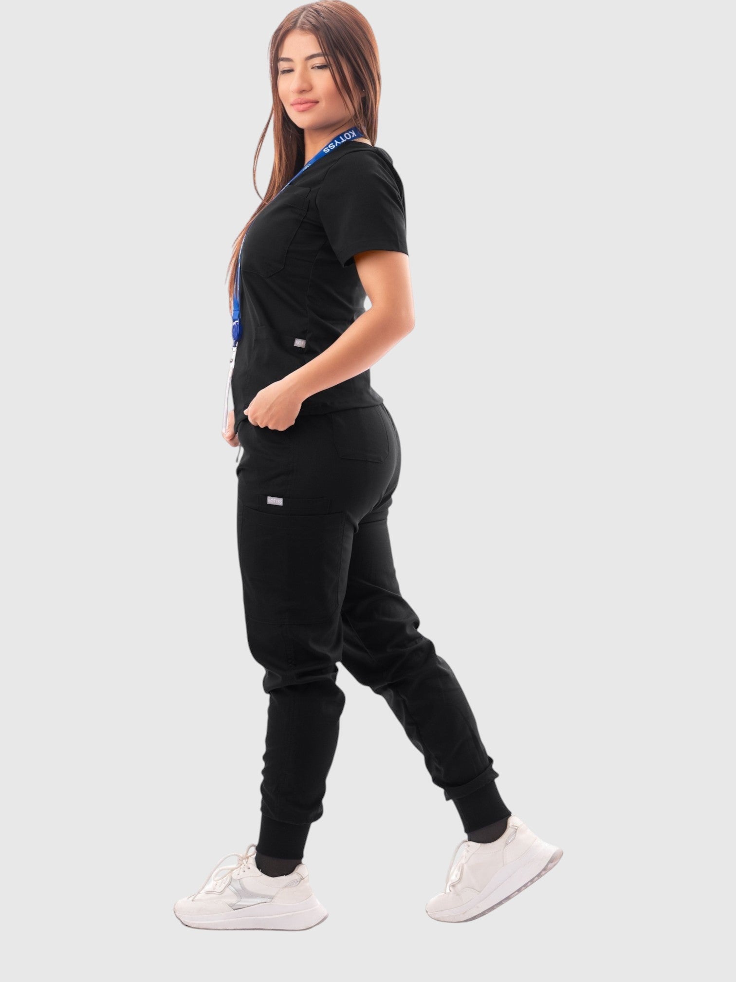 A woman wearing a black Kotyss V-neck scrub top and multi-pocket jogger pants set, side view.