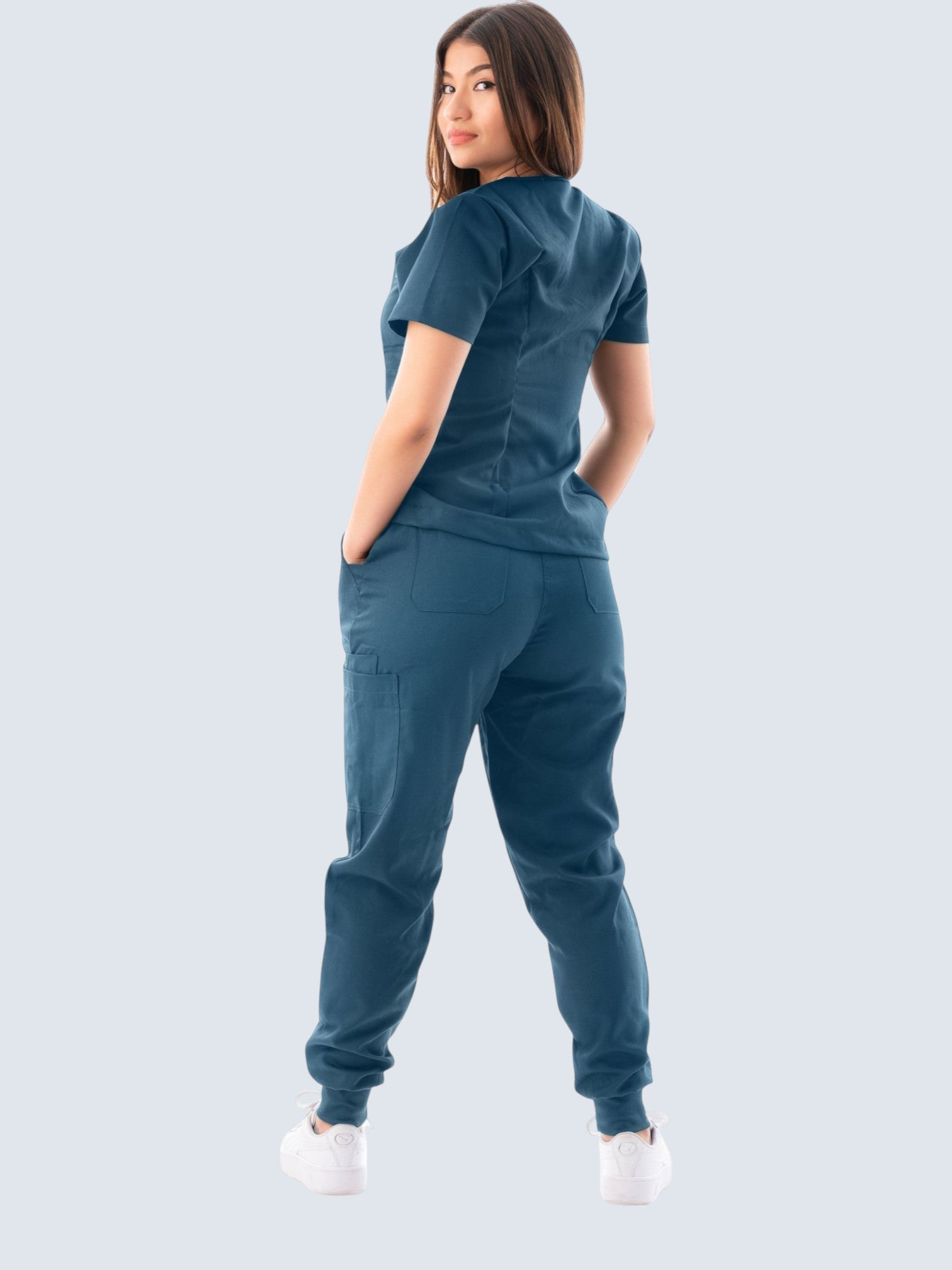 Model wearing a Kotyss blue V-neck scrub top and jogger pants set with multiple pockets, back view.