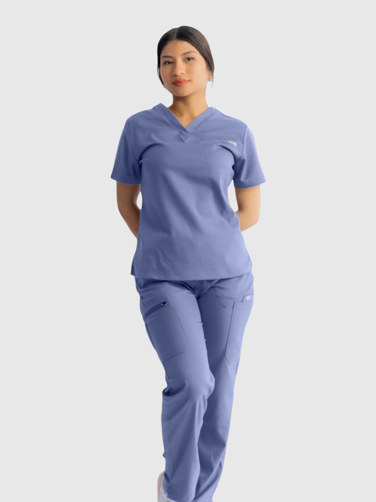 A woman wearing Kotyss blue straight cut medical scrub pants and matching v-neck top with multiple utility pockets.