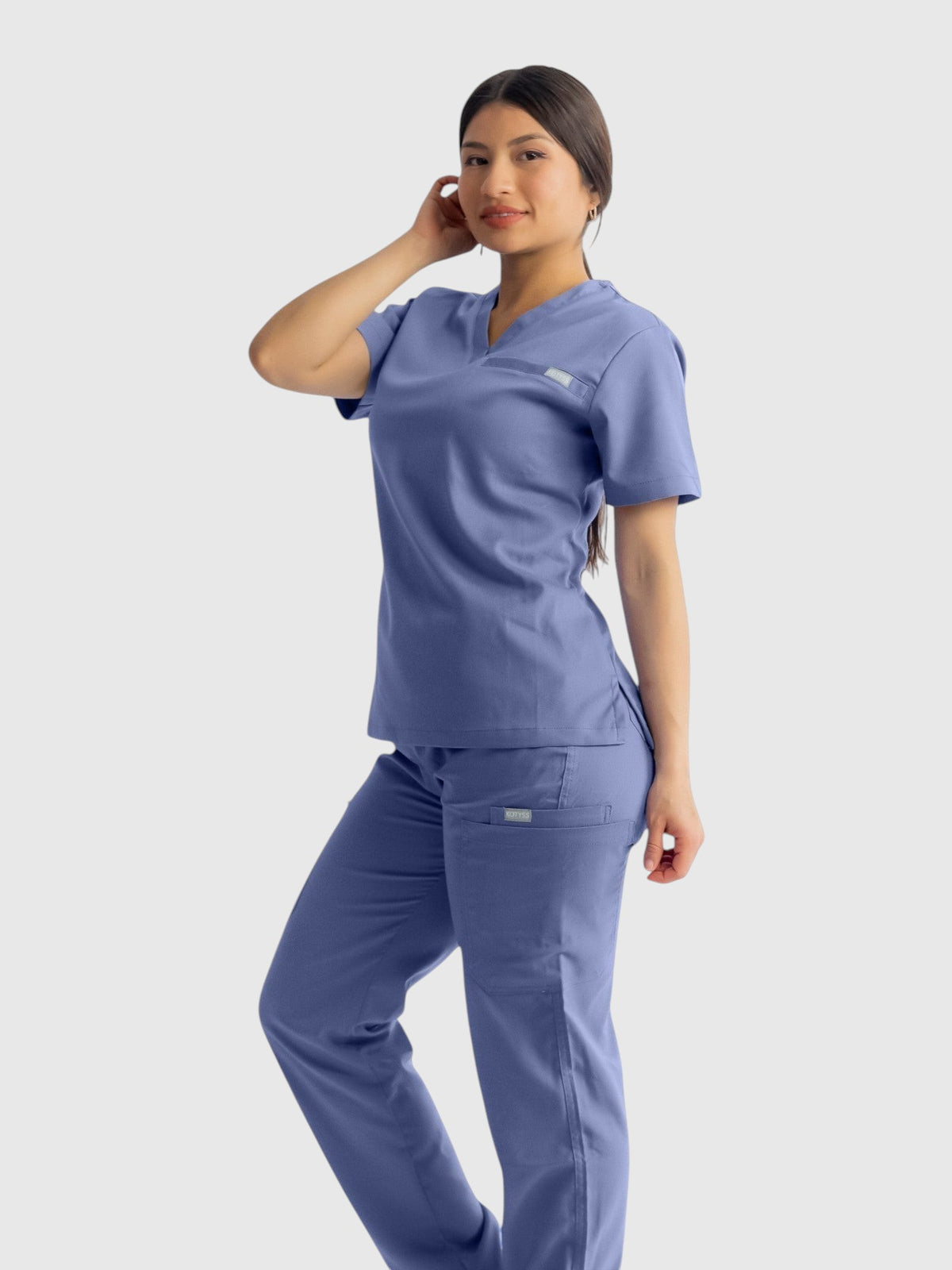 A woman wearing Kotyss blue straight cut medical scrub pants and matching top with multiple utility pockets.