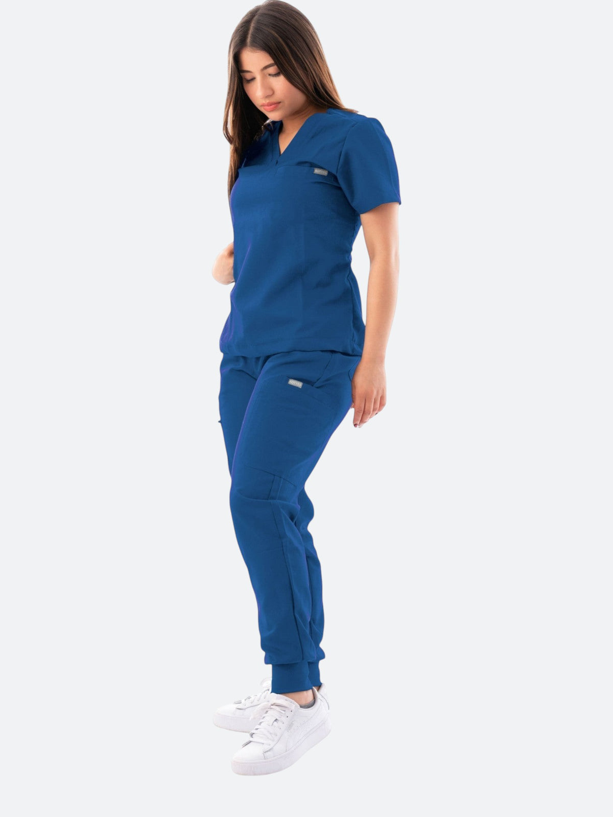 A woman wearing a royal blue Kotyss V-neck scrub top and matching jogger pants with multiple pockets.