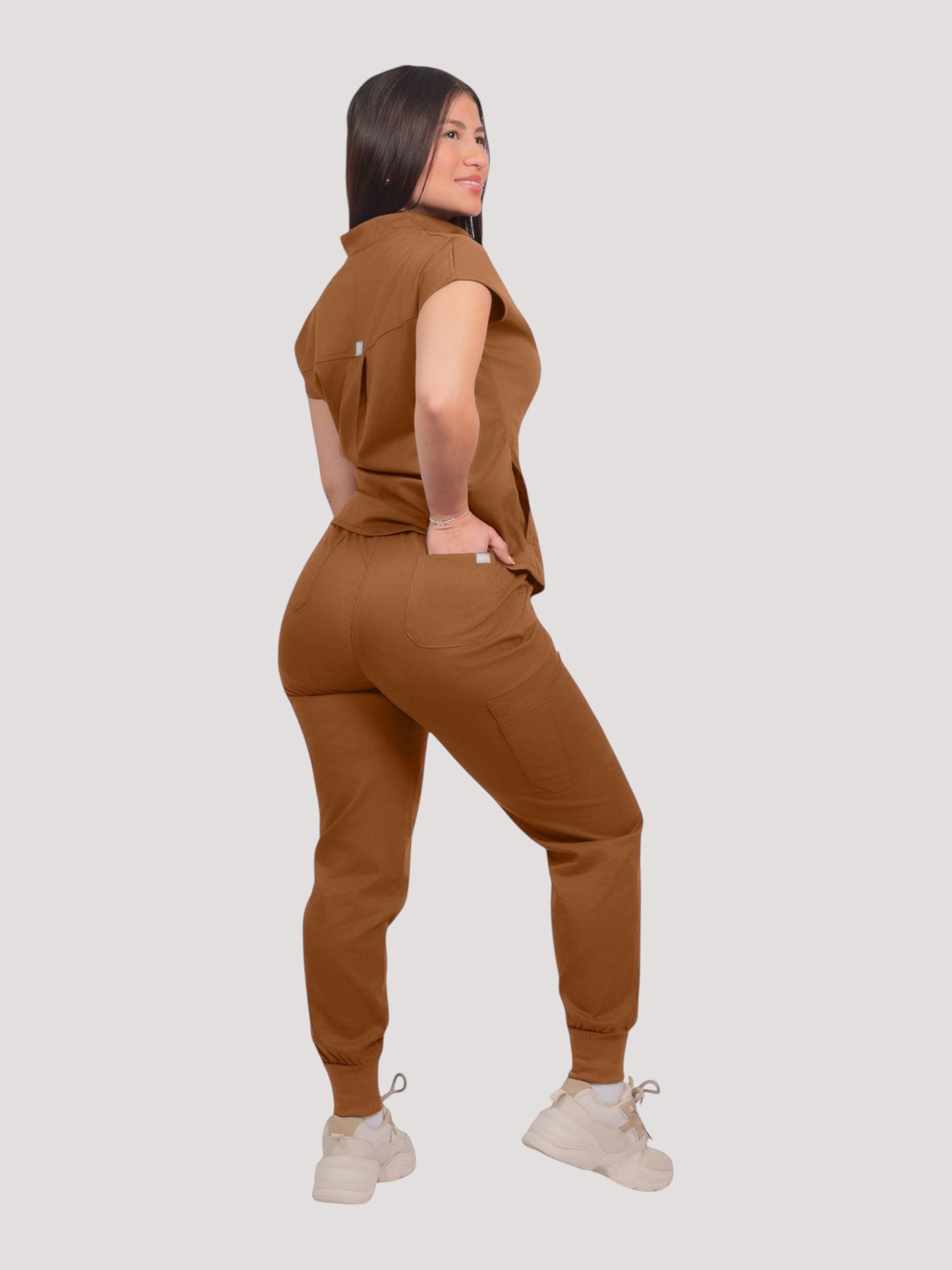 Model wearing a brown Kotyss collared scrub top and matching jogger pants with multiple pockets, rear view