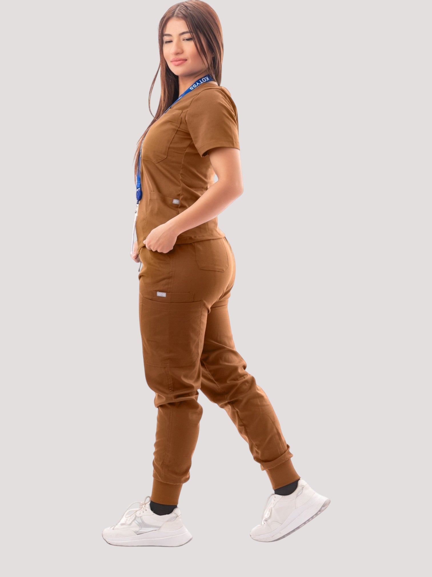 A woman wearing a brown Kotyss V-neck scrub top and jogger pants set with multiple pockets, side view.