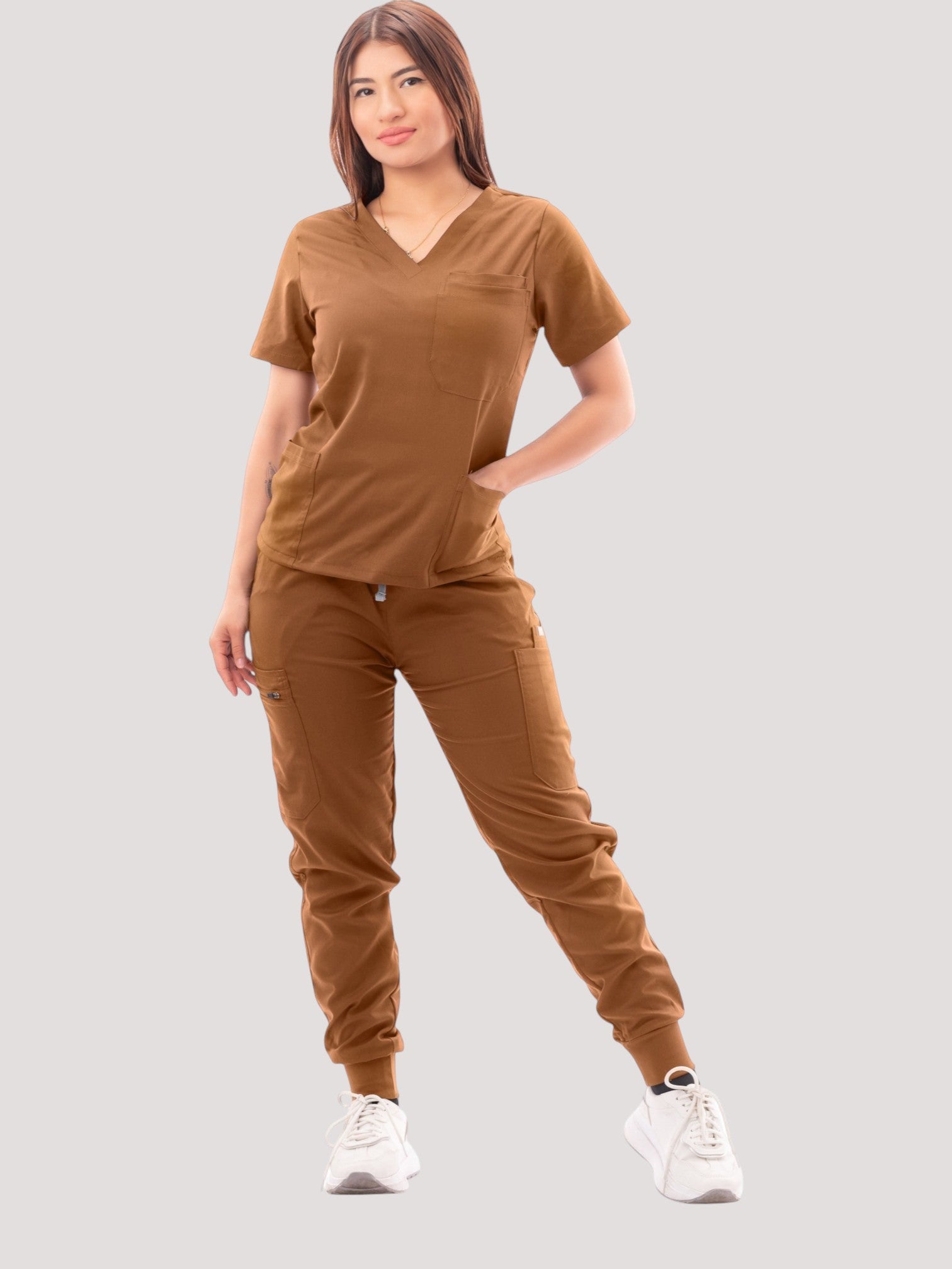 A woman wearing a brown Kotyss V-neck scrub top and matching multi-pocket jogger pants with white sneakers.