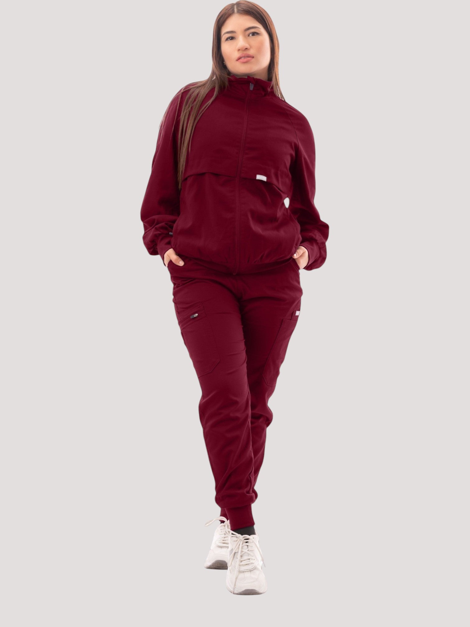 A woman wearing a burgundy Kotyss scrub jacket with a high neck, ribbed cuffs, and matching scrub pants.