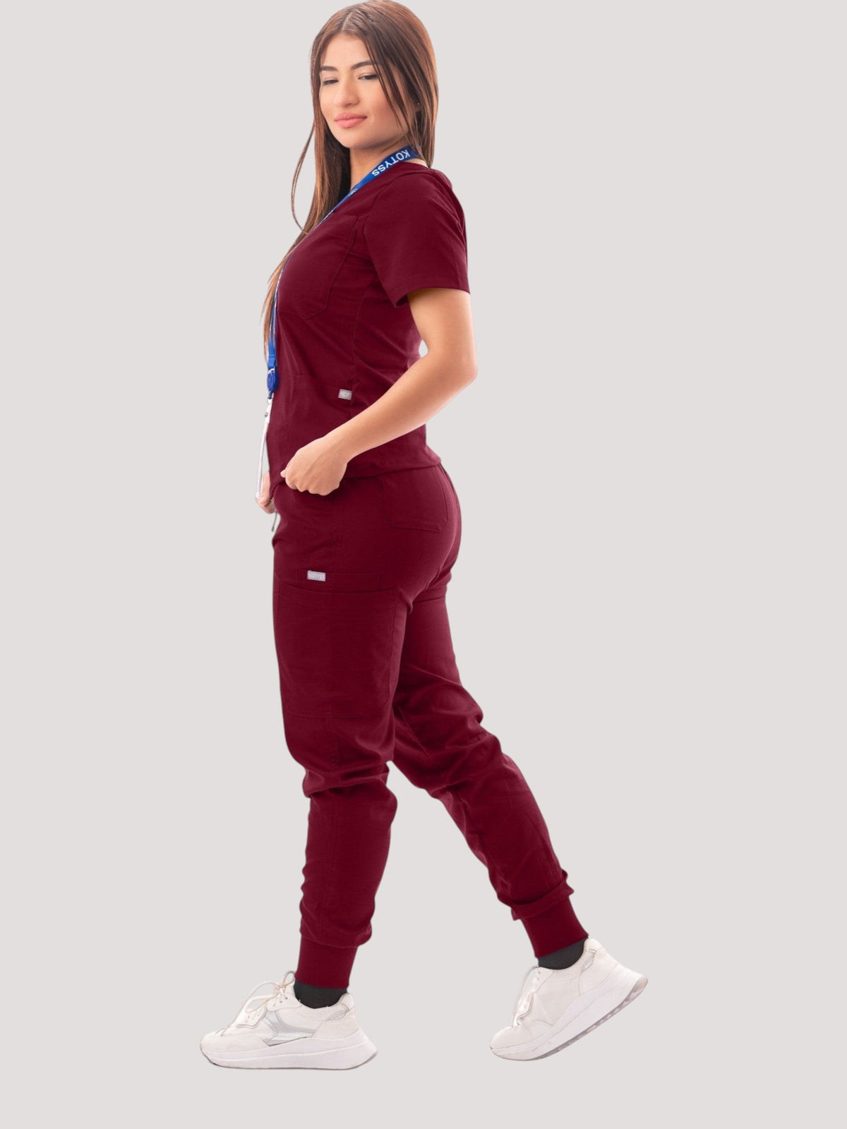 Woman wearing a Kotyss burgundy V-neck scrub top and multi-pocket jogger pants set with white sneakers