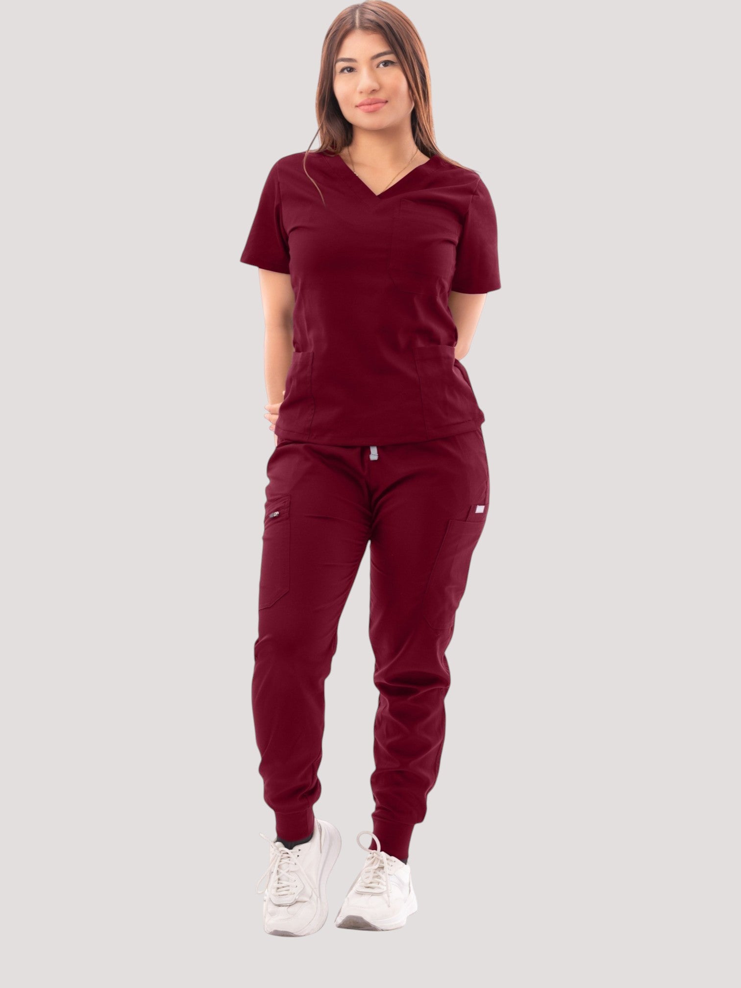 Woman wearing a burgundy Kotyss V-neck scrub top and matching multi-pocket jogger pants with white sneakers.
