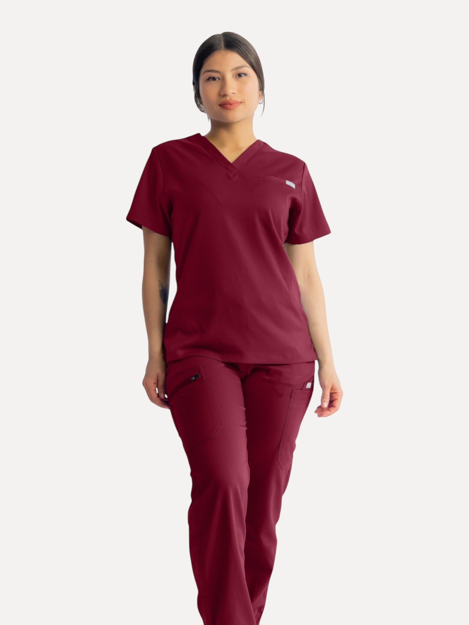 A healthcare professional wearing Kotyss burgundy straight cut scrub pants and matching V-neck scrub top.
