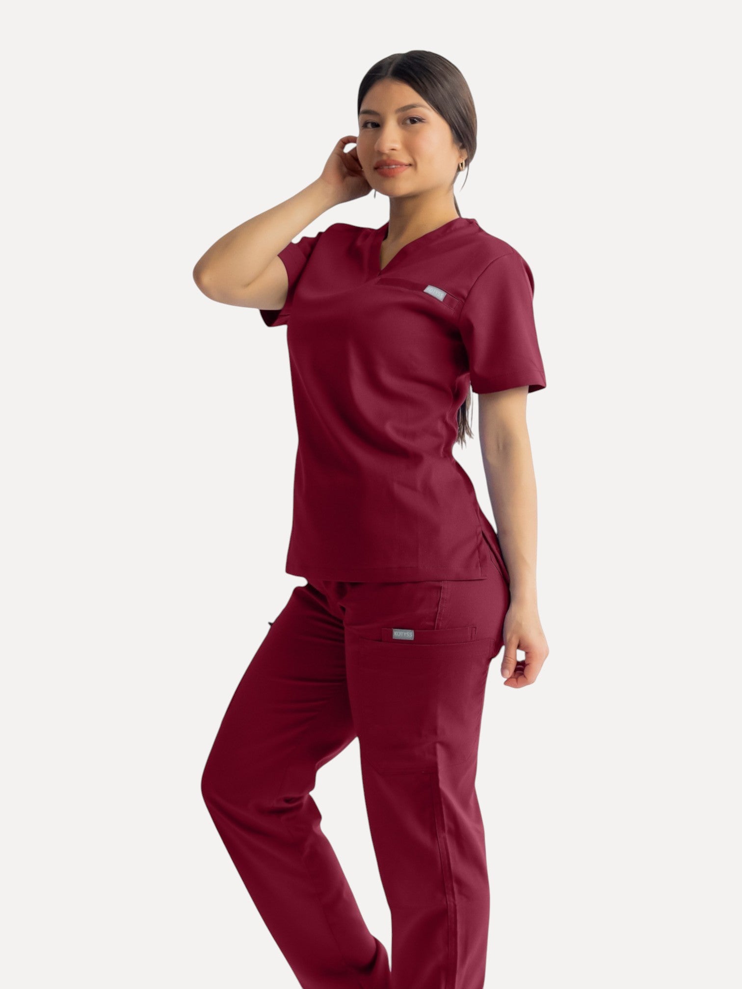 A model wearing Kotyss burgundy straight cut medical scrub pants and matching top with multiple utility pockets.