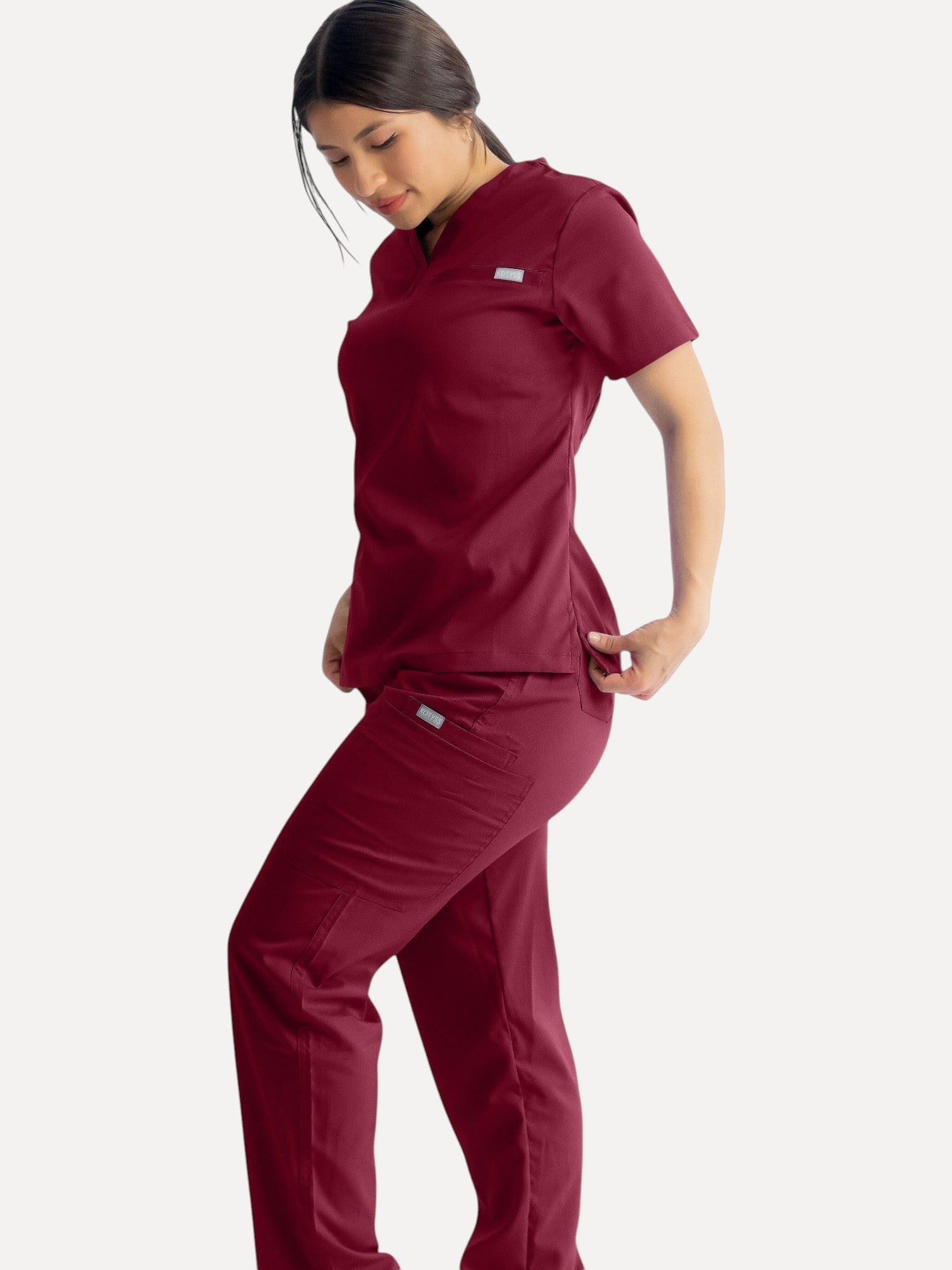 A woman wearing Kotyss burgundy straight cut medical scrub pants and matching top, featuring 4-way stretch fabric.