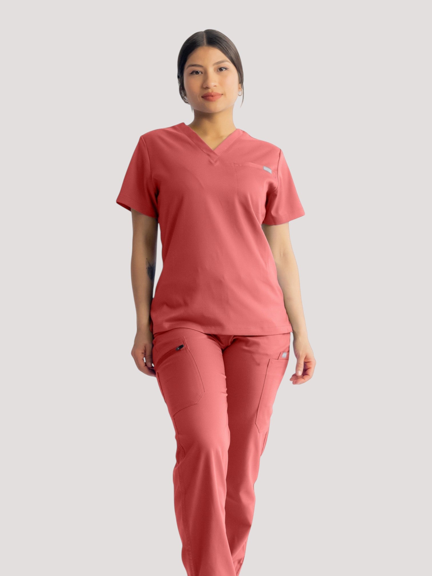 A healthcare professional wearing Kotyss coral pink straight cut scrub pants and matching V-neck scrub top