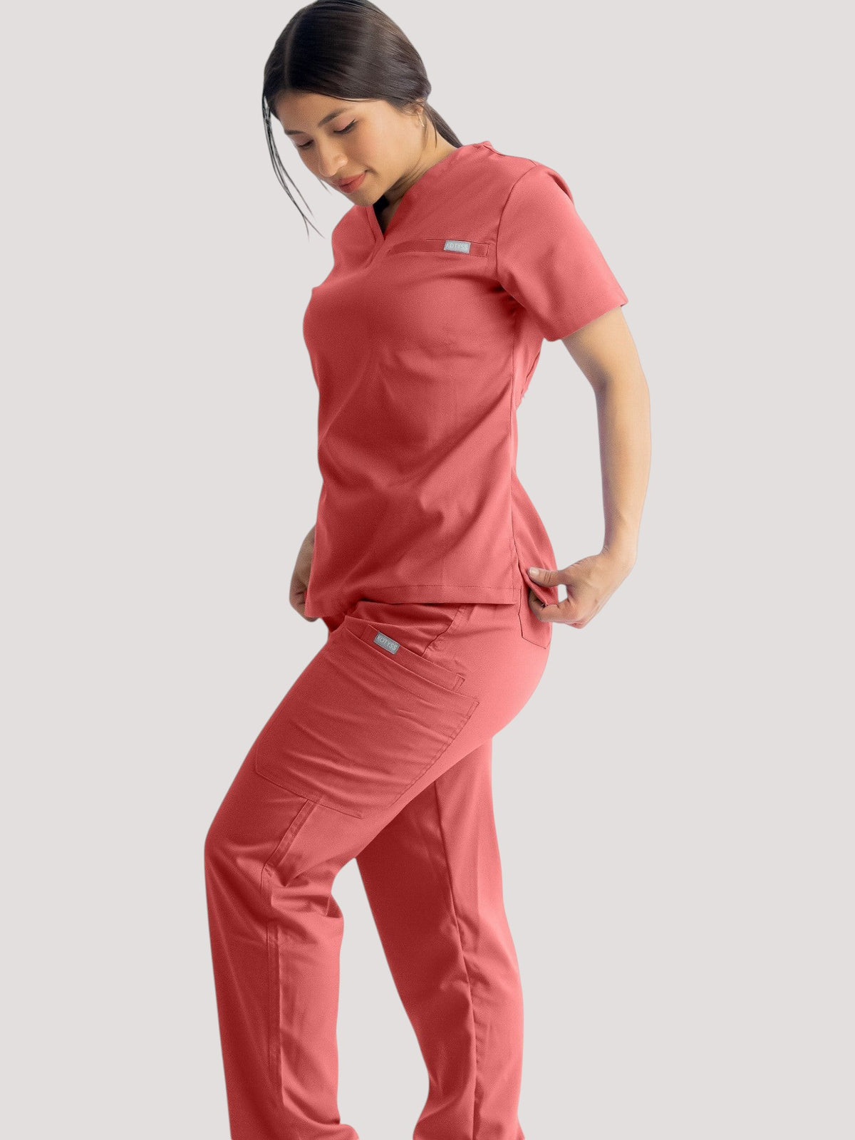 A woman wearing Kotyss coral pink straight cut medical scrub pants and matching top with multiple utility pockets.
