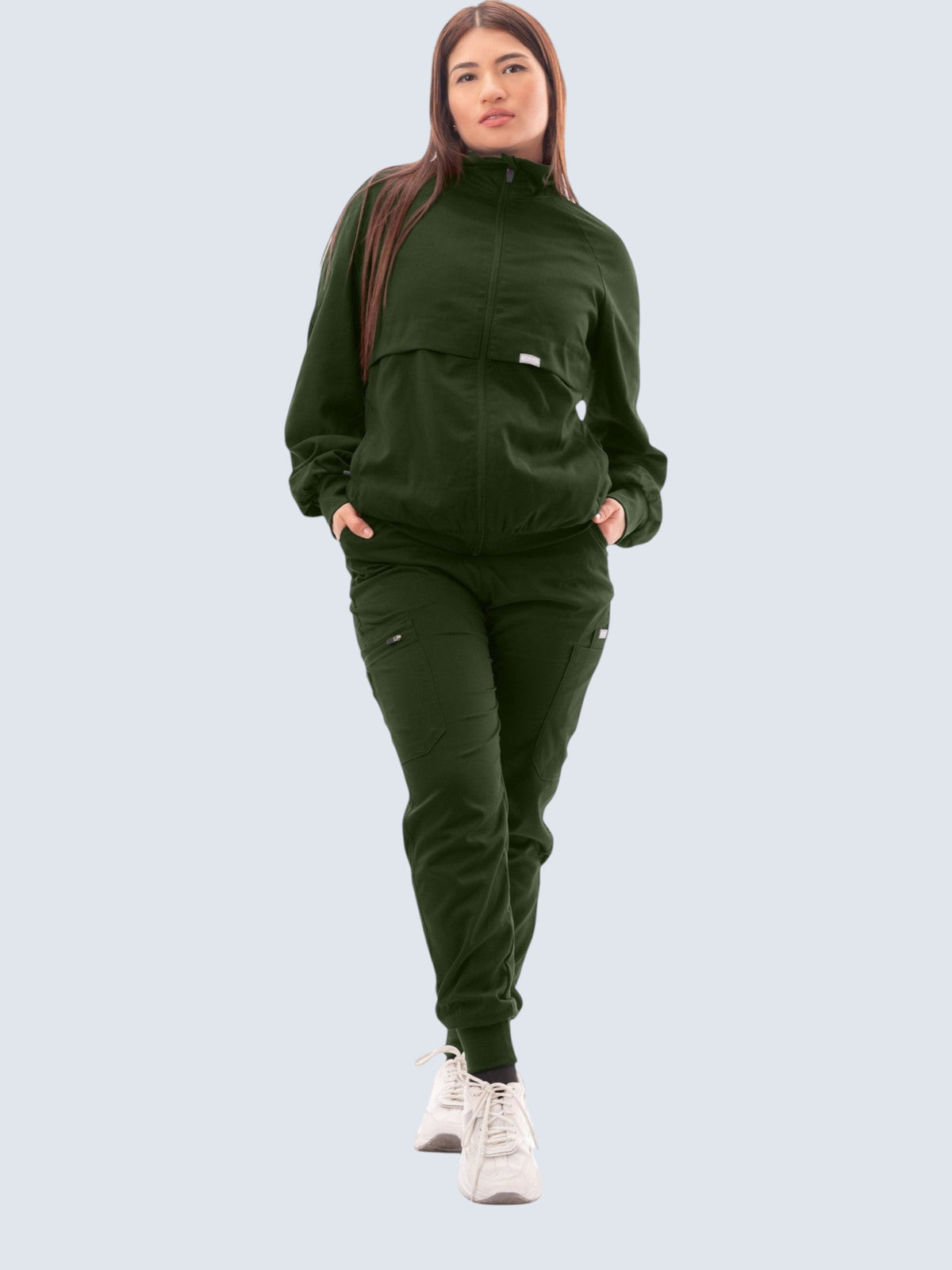 A woman wearing a Kotyss dark green scrub jacket with a high neck and matching scrub pants in a professional setting.